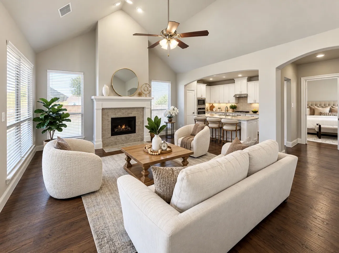 Vaulted ceiling with a ceiling fan and recessed lighting, wood-finish flooring, fireplace with a tiled surround and mantel, arched doorways, and a kitchen with an island and built-in appliances