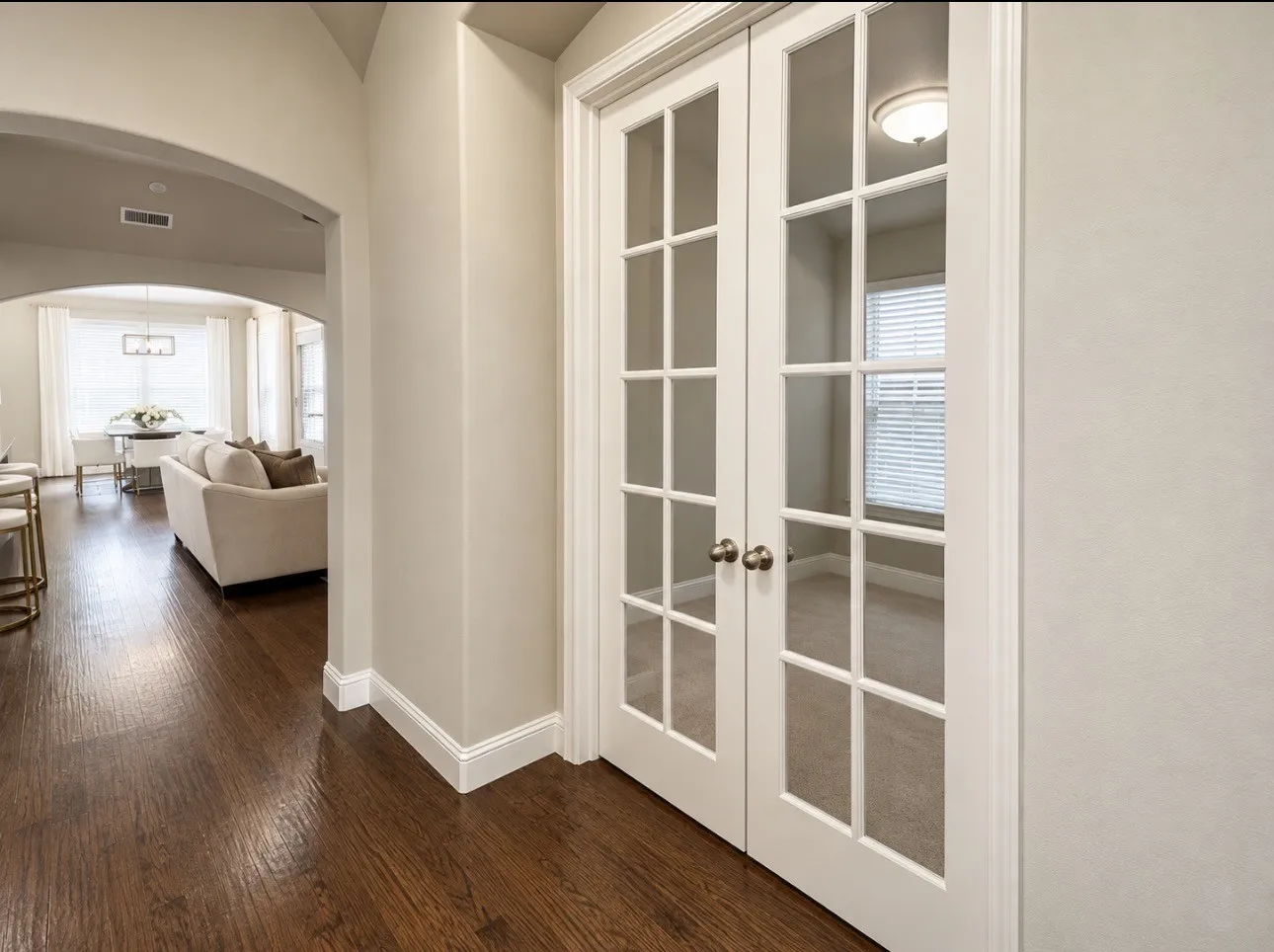 Rich wood-finish flooring, arched doorway, white trim, and French doors