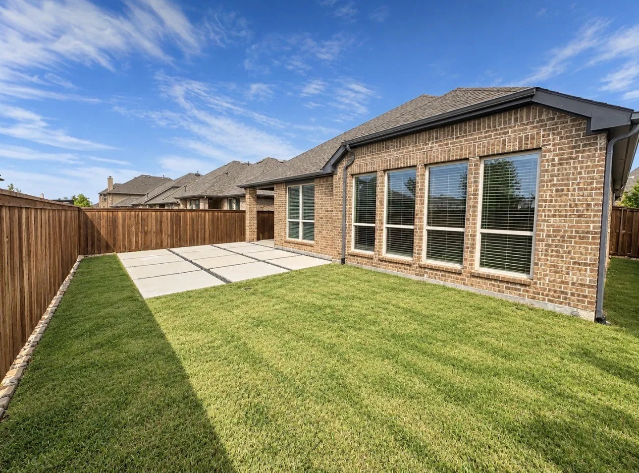 Brick exterior with multiple windows, leading to a concrete patio and a manicured lawn