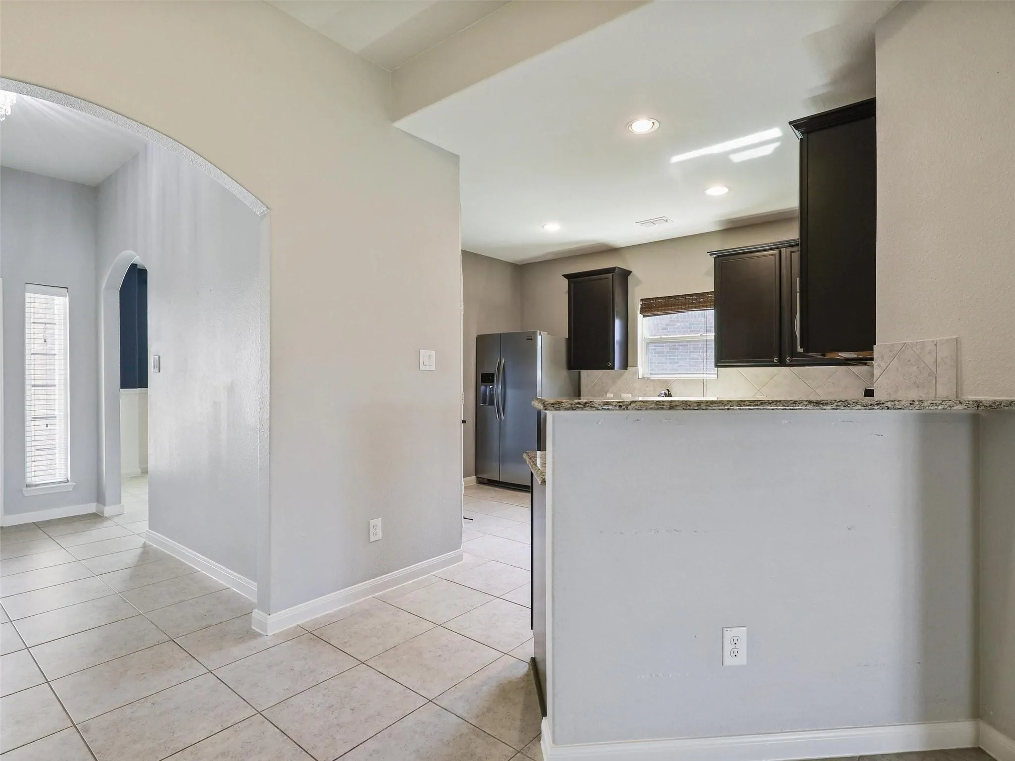 Archway entry, light-colored tile flooring, dark wood-finish cabinetry, recessed lighting, and granite-style countertops