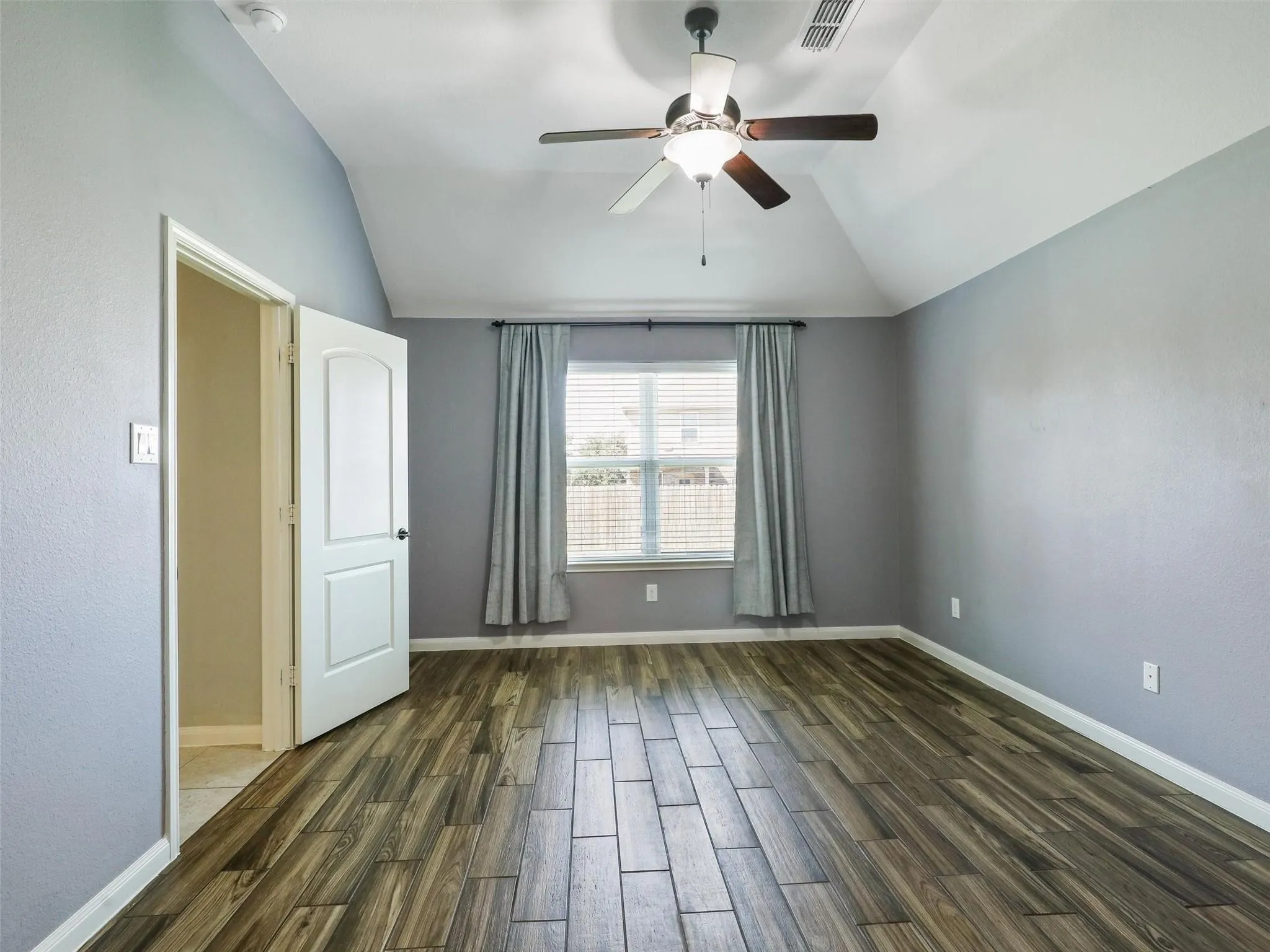 Vaulted ceiling, wood-finish flooring, ceiling fan, window with blinds, and paneled door