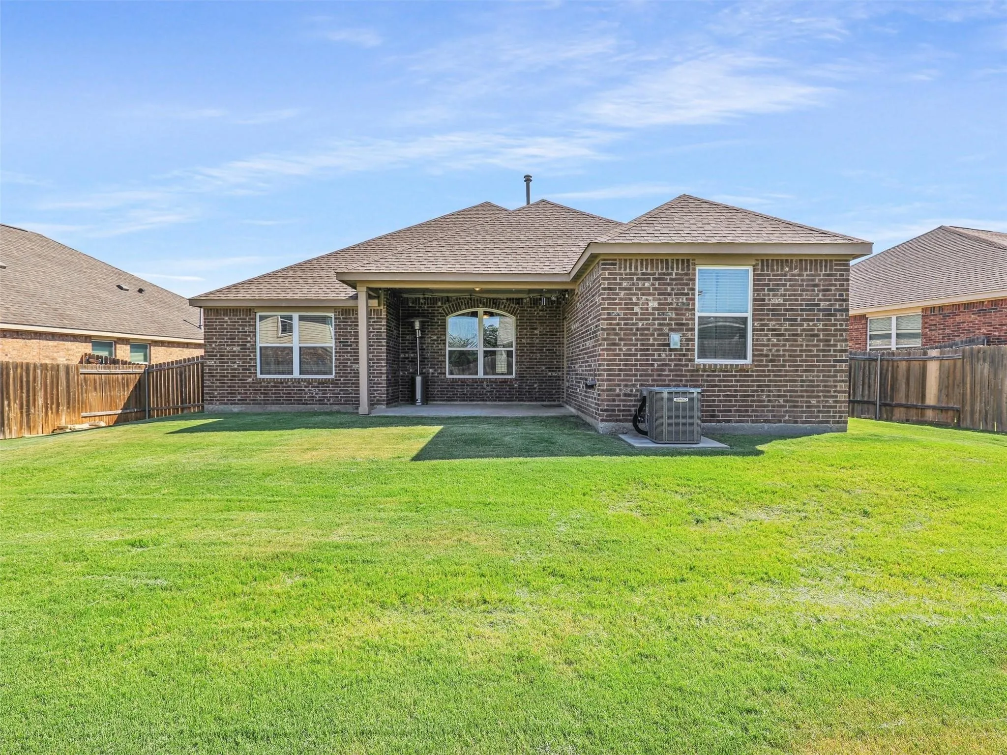 Expansive backyard with a manicured lawn, brick exterior, and covered patio