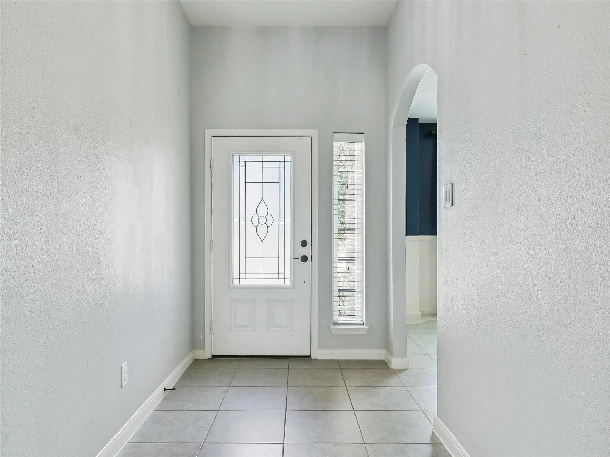 Entryway featuring a white door with decorative glass, a sidelight with blinds, tile flooring, and an arched doorway