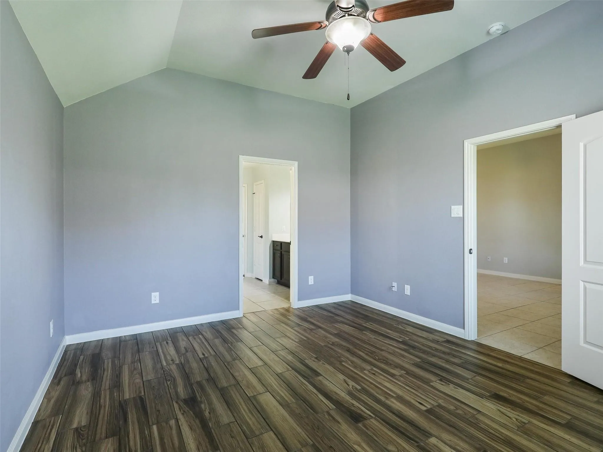 Vaulted ceiling, wood-finish flooring, ceiling fan with integrated lighting, paneled interior doors, and a neutral wall palette