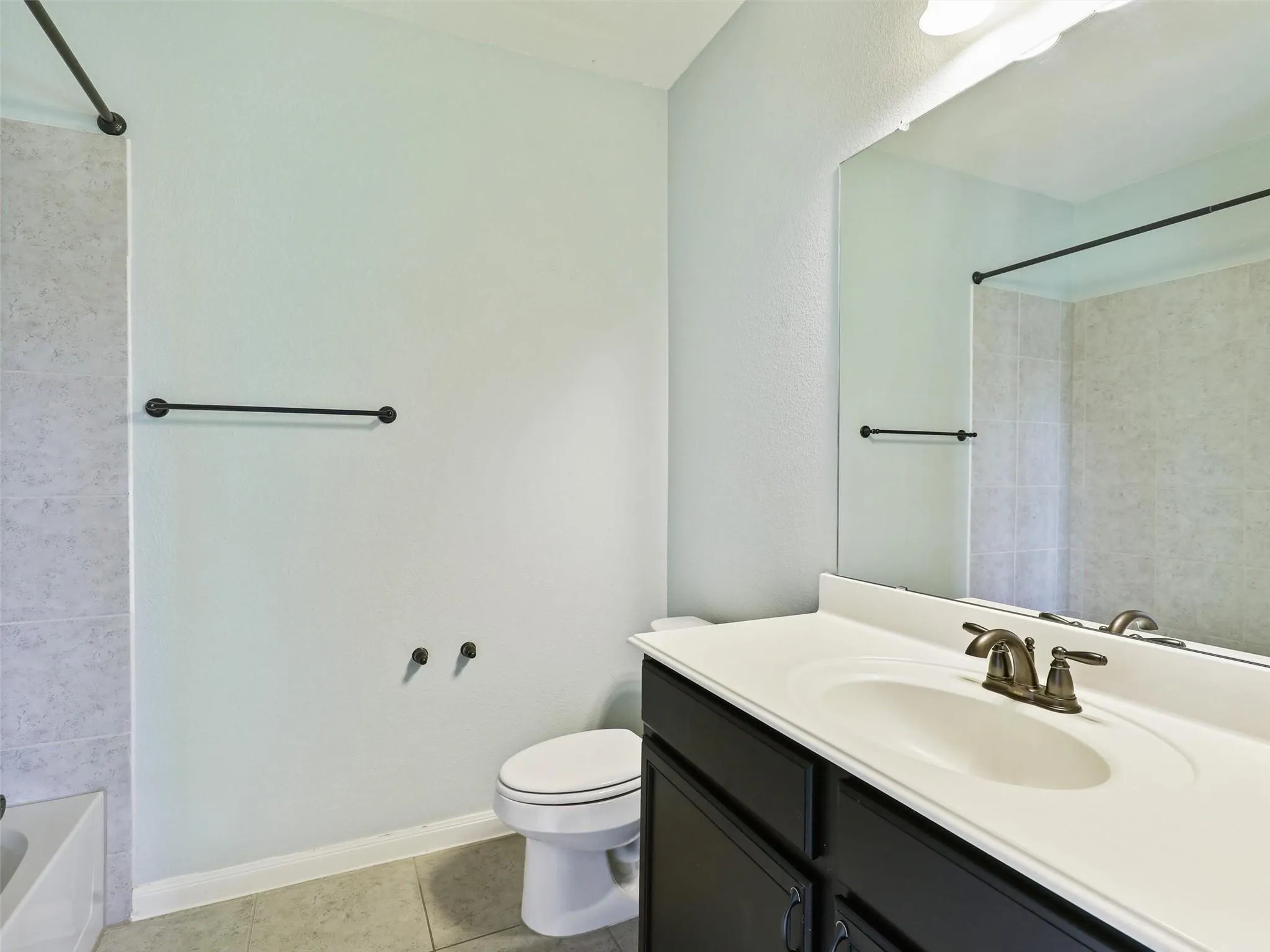 Bathroom featuring a shower-tub combination, a vanity with a dark wood-finish cabinet, and a large wall-mounted mirror