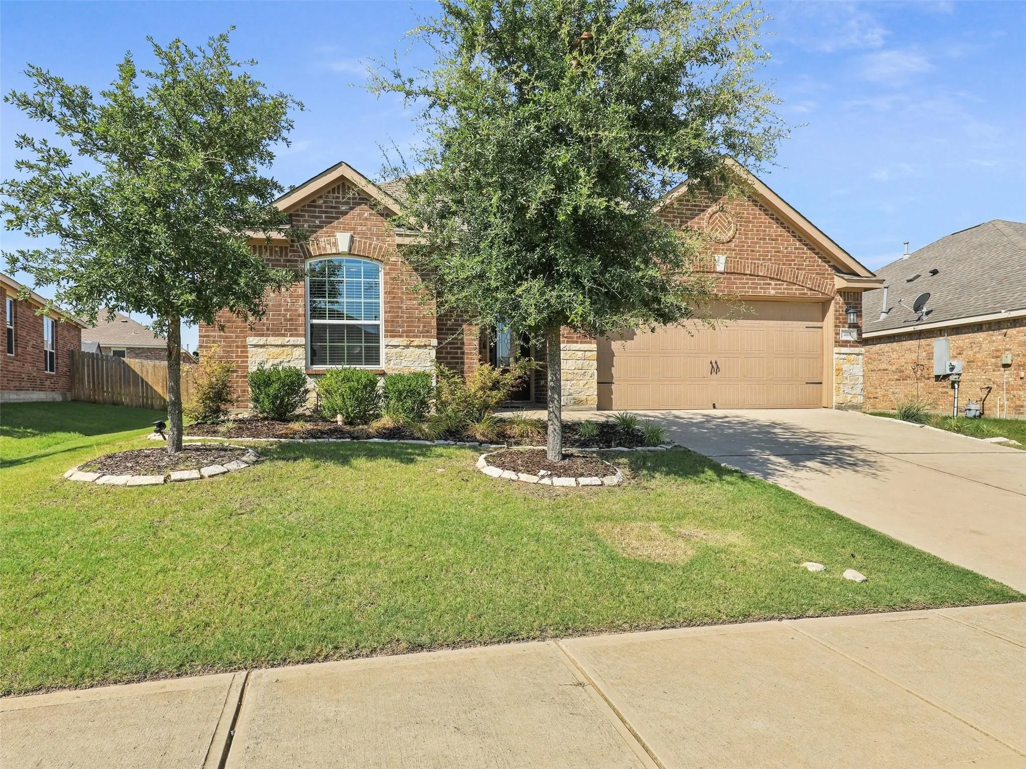 Brick exterior with stone accents, arched window, attached two-car garage, concrete driveway, and established front yard landscaping