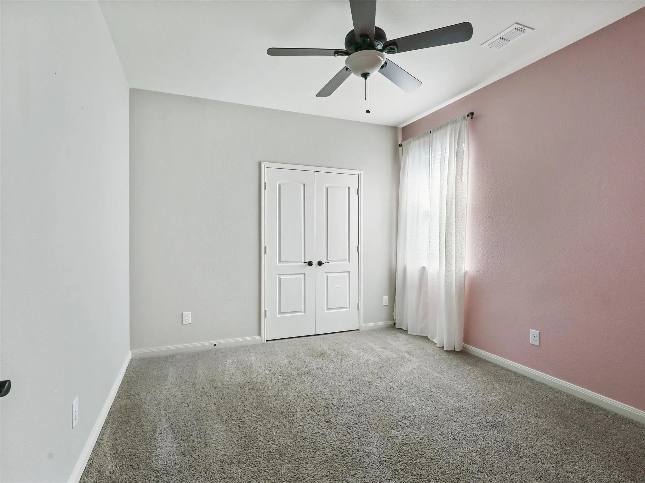 Plush carpeting, ceiling fan, double doors, window with curtain rod, and neutral wall tones