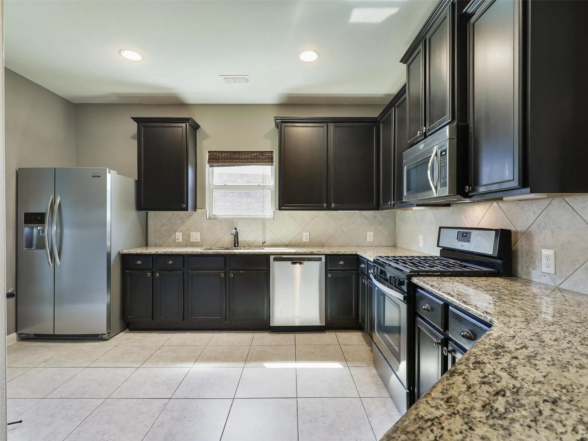 Kitchen featuring dark wood cabinetry, granite countertops, tile flooring, stainless steel appliances, and a tile backsplash