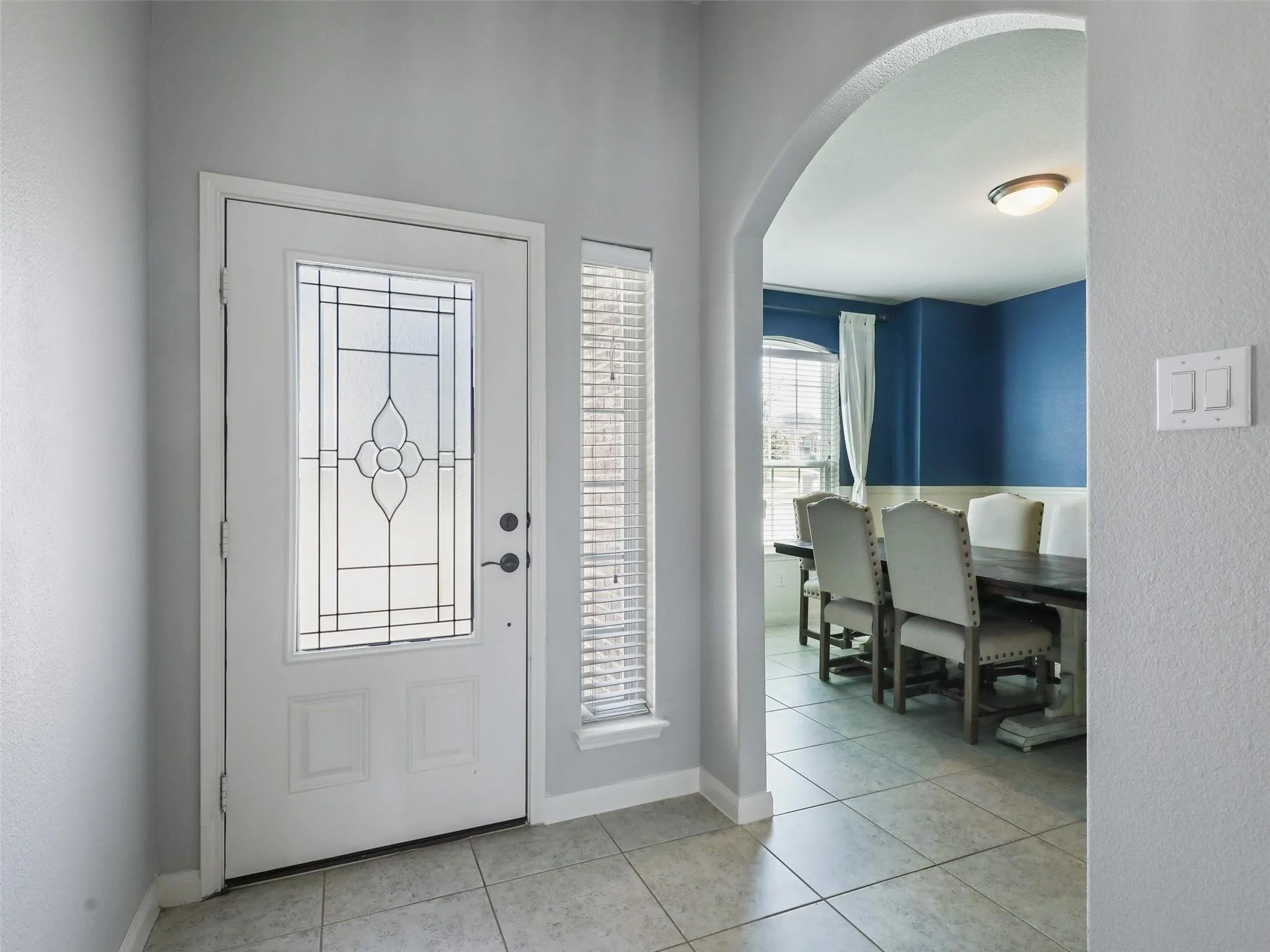 Entryway featuring a decorative glass door, side window with blinds, and tile flooring