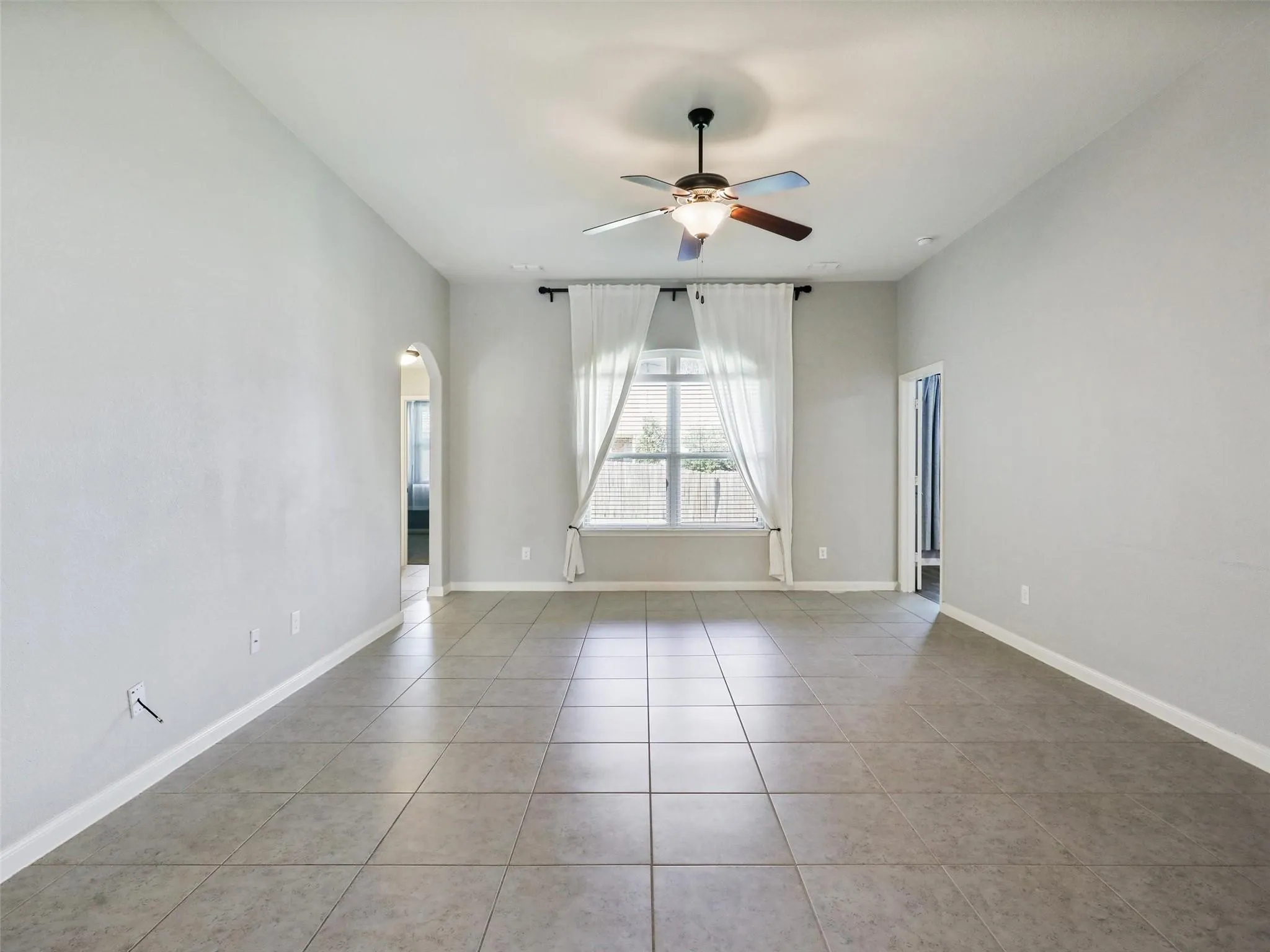Recessed ceiling with a central fan light fixture, arched doorway, and tiled flooring