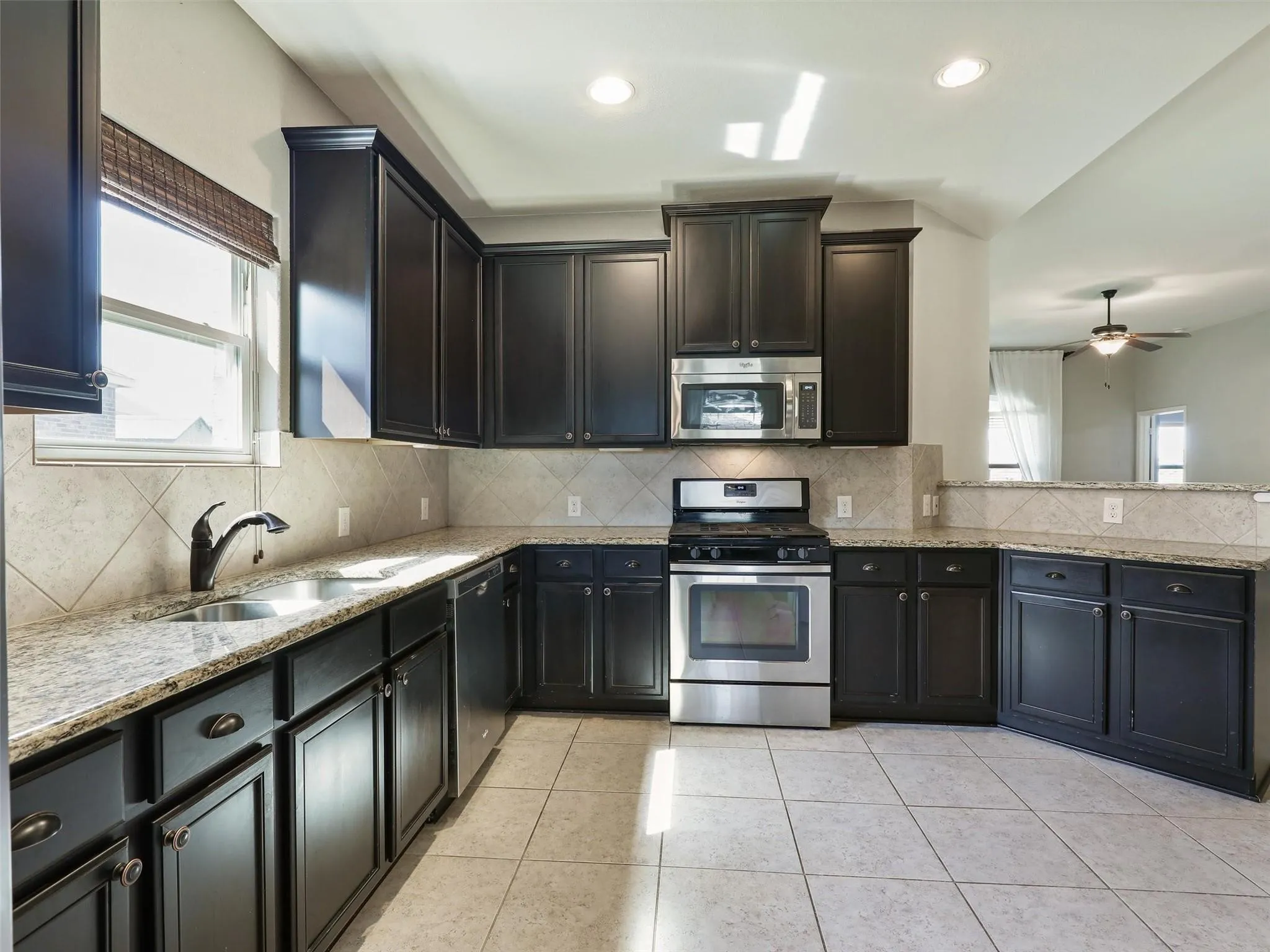 Kitchen featuring dark wood cabinetry, stainless steel appliances, tile flooring, granite countertops, and a tile backsplash