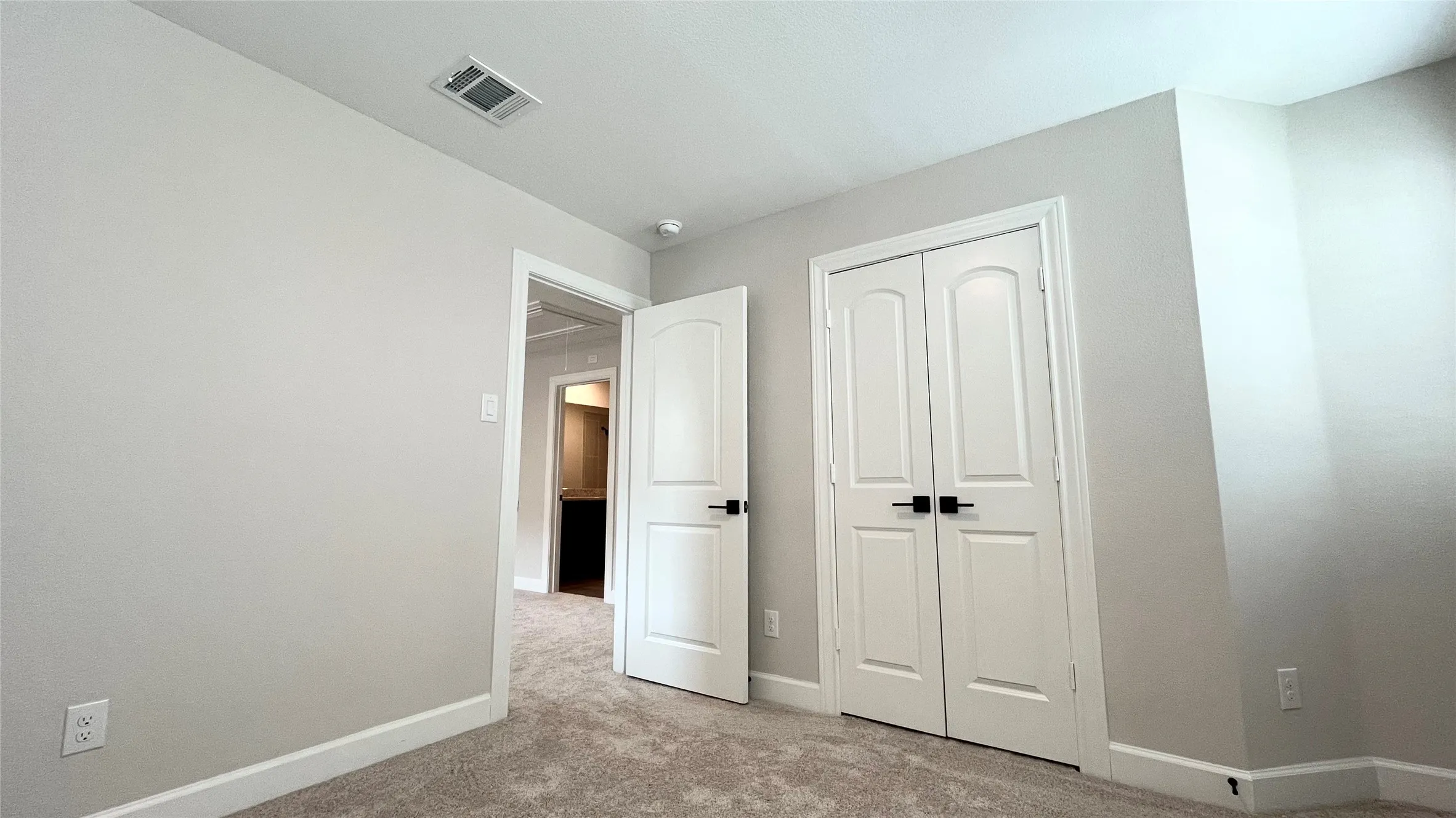 Carpeted flooring with light-toned walls, white trim, and a white interior door with black hardware