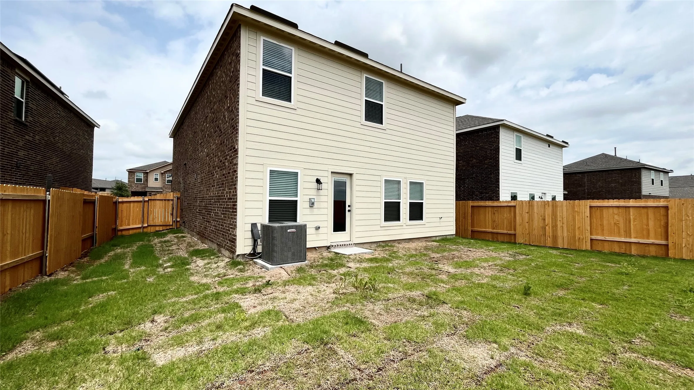 Expansive grass-covered yard featuring a two-story exterior with siding and brick, a rear entry door, and a full privacy fence
