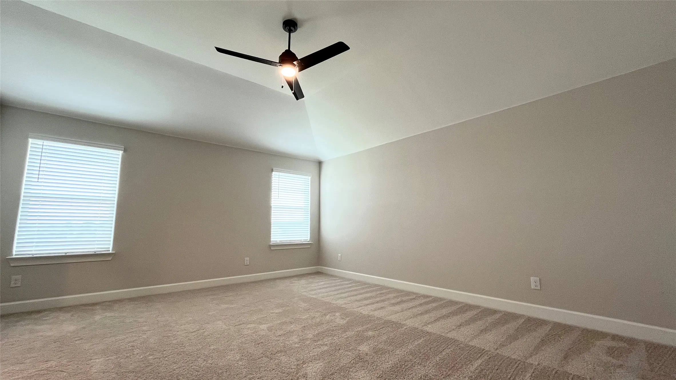 Vaulted ceiling with a ceiling fan, two windows with blinds, and neutral-toned carpet