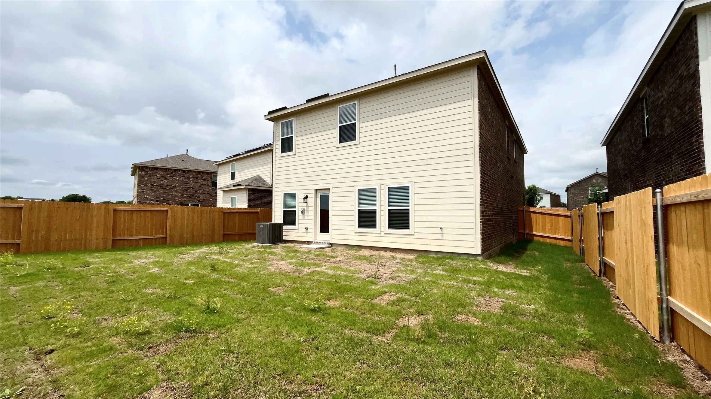 Expansive rear yard featuring wood privacy fencing, a ground-level patio, and a two-story exterior with siding and brick accents