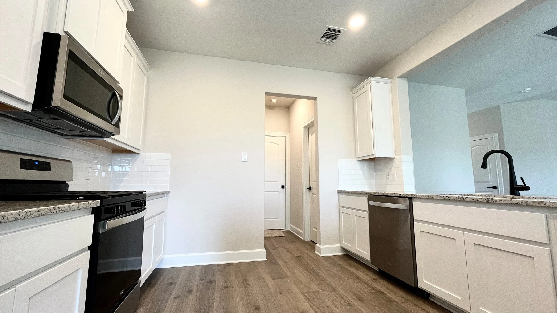 Kitchen featuring granite countertops, white cabinetry, stainless steel appliances, wood-finish flooring, and a subway tile backsplash