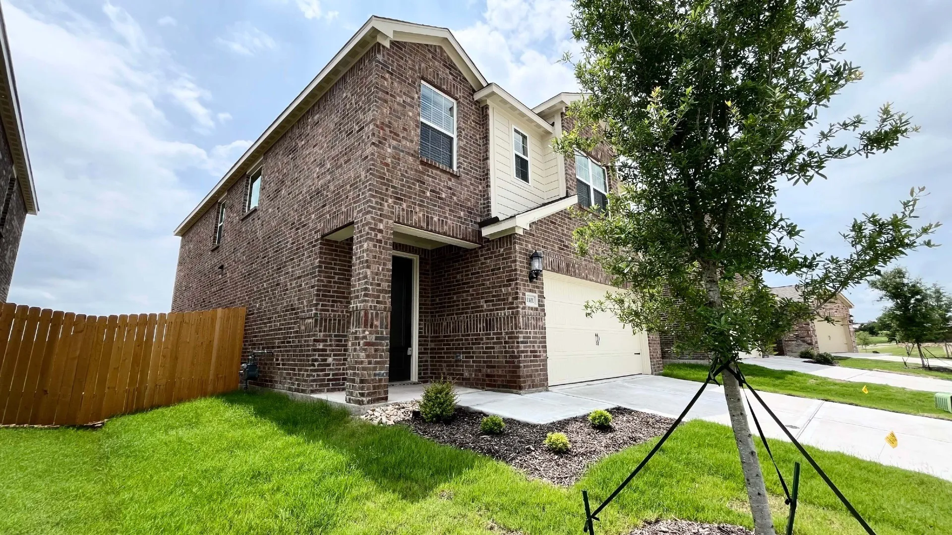Two-story brick exterior with light-colored siding accents, an attached garage, a covered entryway, and a fenced yard