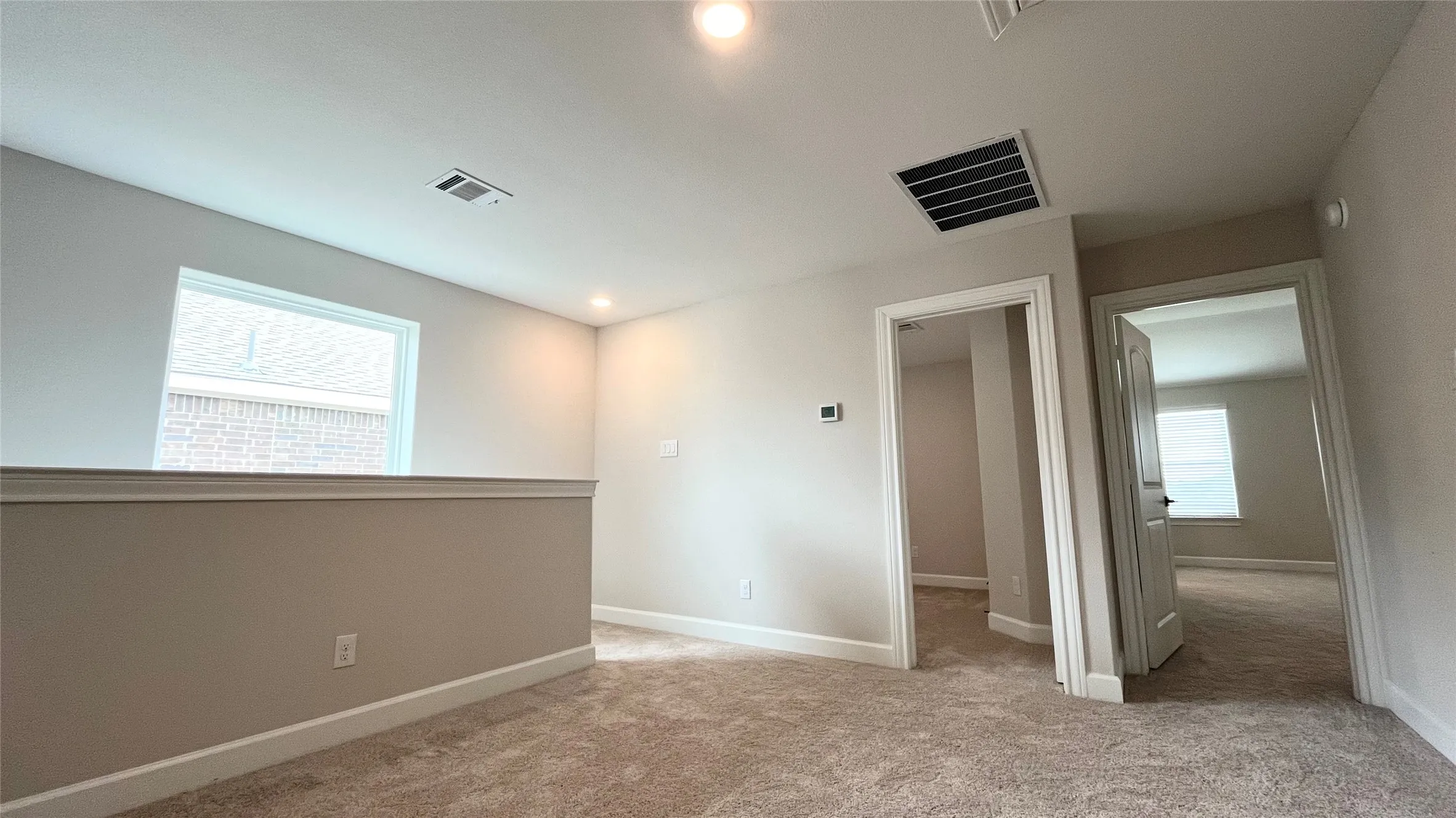 Carpeted upper-level landing with neutral wall tones, recessed lighting, and a white framed window