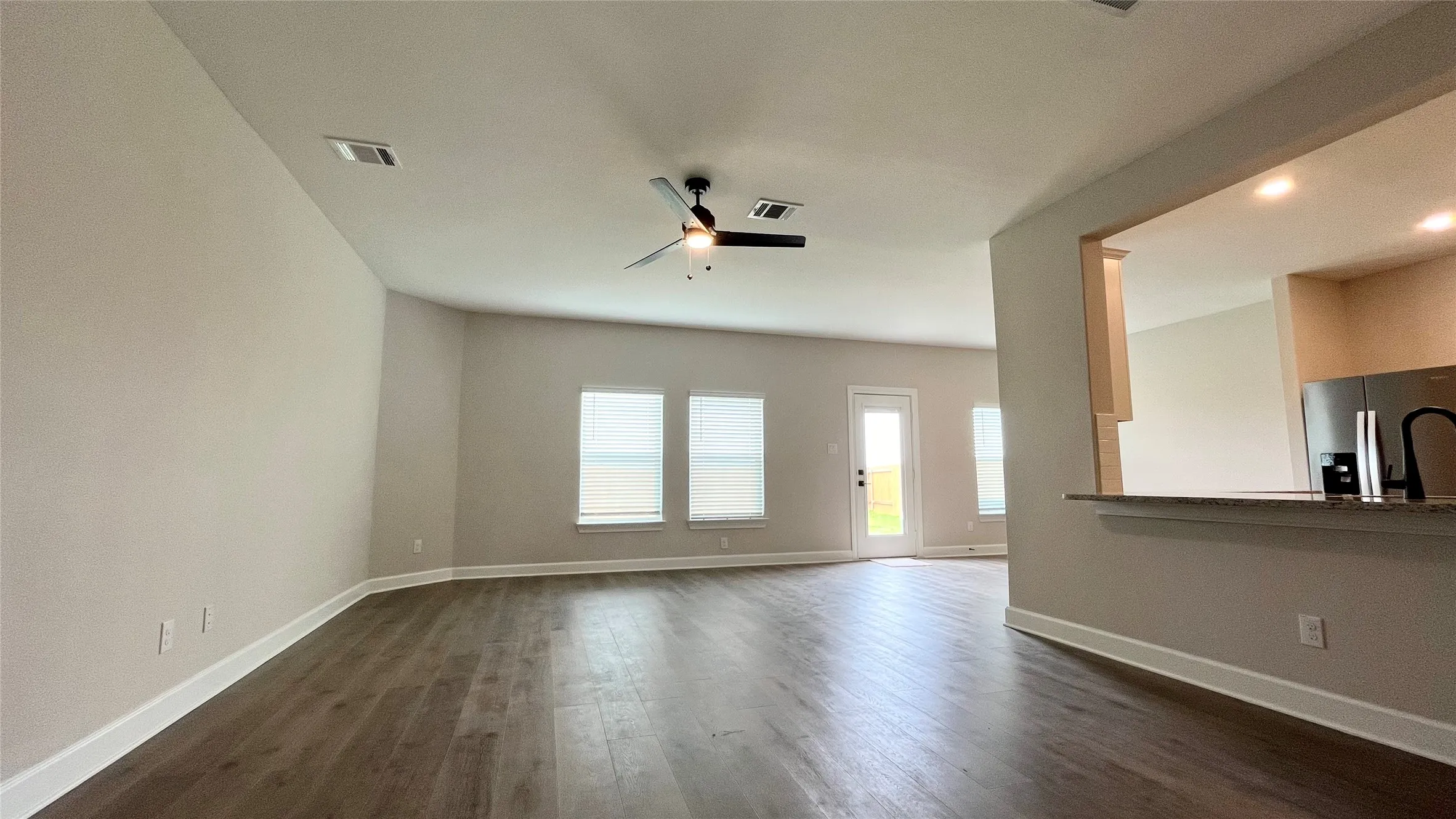 Spacious interior featuring wood-finish flooring, multiple windows, a ceiling fan, and a kitchen pass-through with a breakfast bar