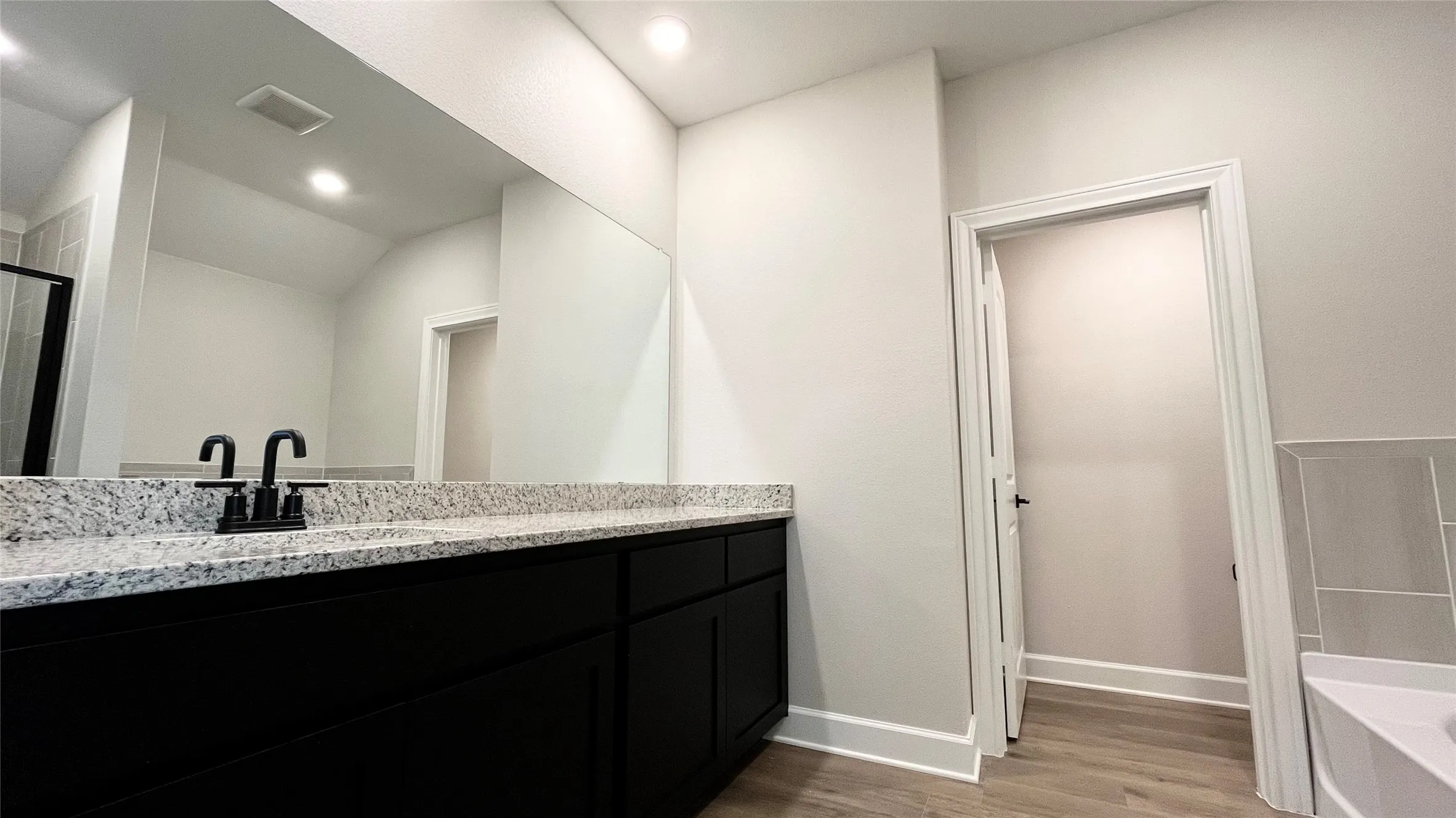 Dark wood-finish vanity with ample storage, light-toned speckled countertop, and matte black fixtures