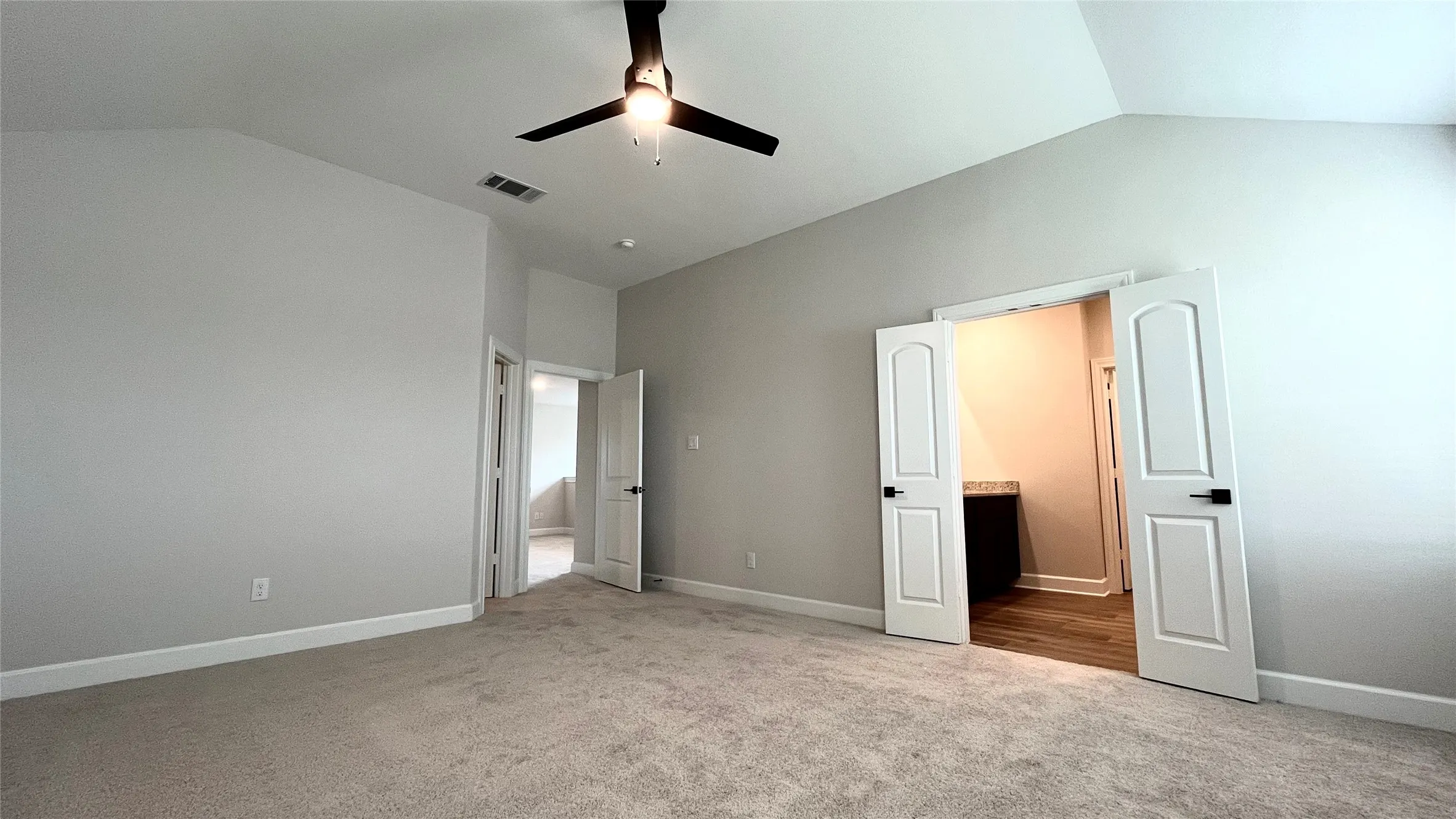 Carpeted flooring, vaulted ceiling with a ceiling fan, light-colored walls, and white interior doors with black hardware