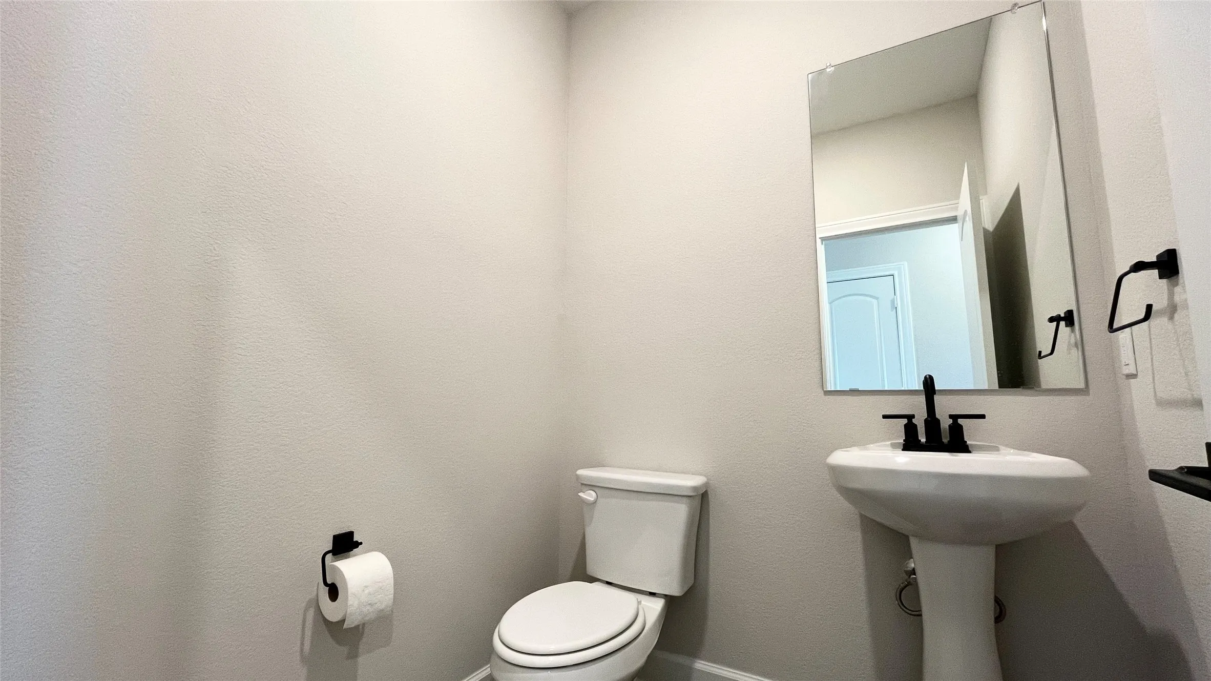 Pedestal sink with a matte black faucet, wall-mounted mirror, and white toilet