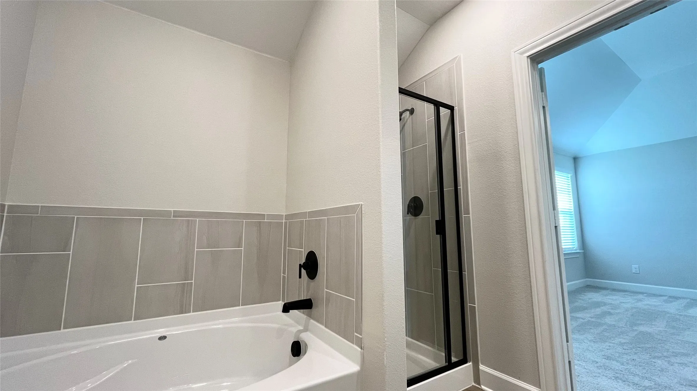 Corner soaking tub with matte black fixtures, an adjacent walk-in shower with a glass enclosure, and modern tile surround