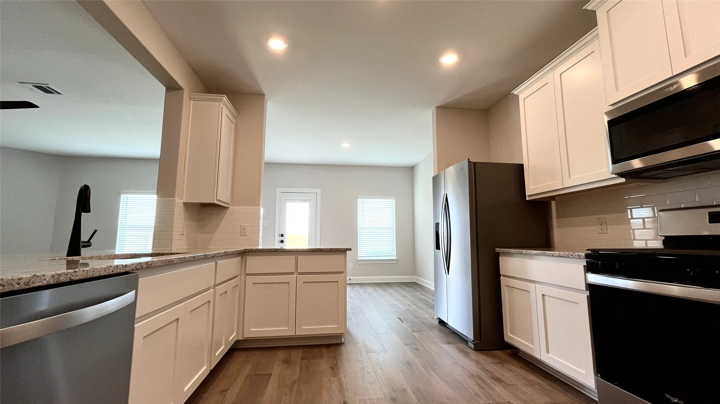 Kitchen featuring white shaker-style cabinetry, stainless steel appliances, granite countertops, and wood-finish flooring