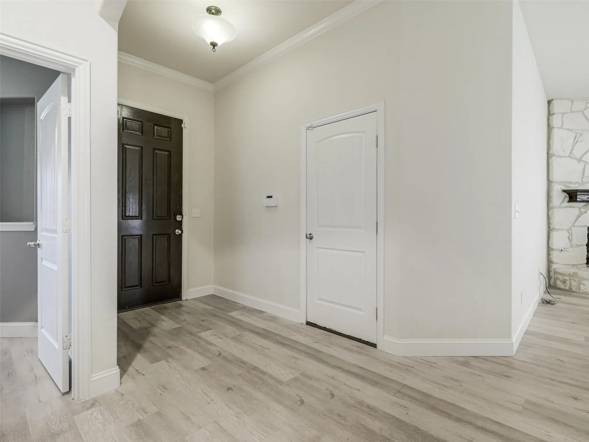 Wood-finish flooring, white baseboards, crown molding, a dark paneled entry door, and a stone-clad fireplace