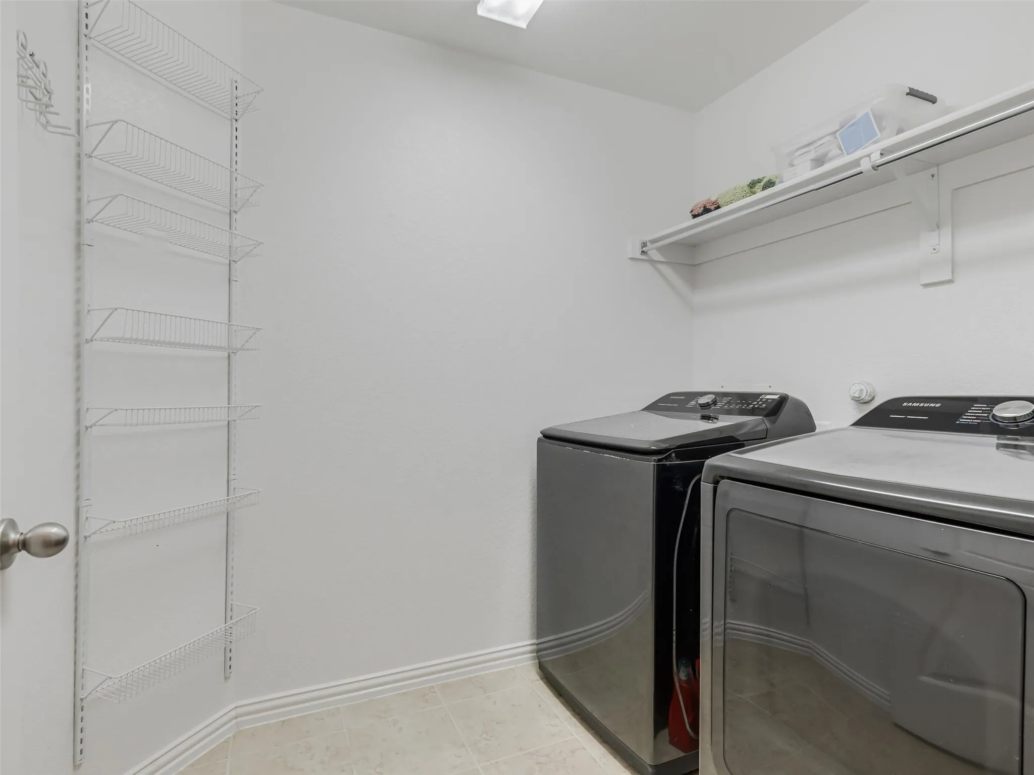Utility room featuring wire shelving, a wall-mounted shelf, and tiled flooring