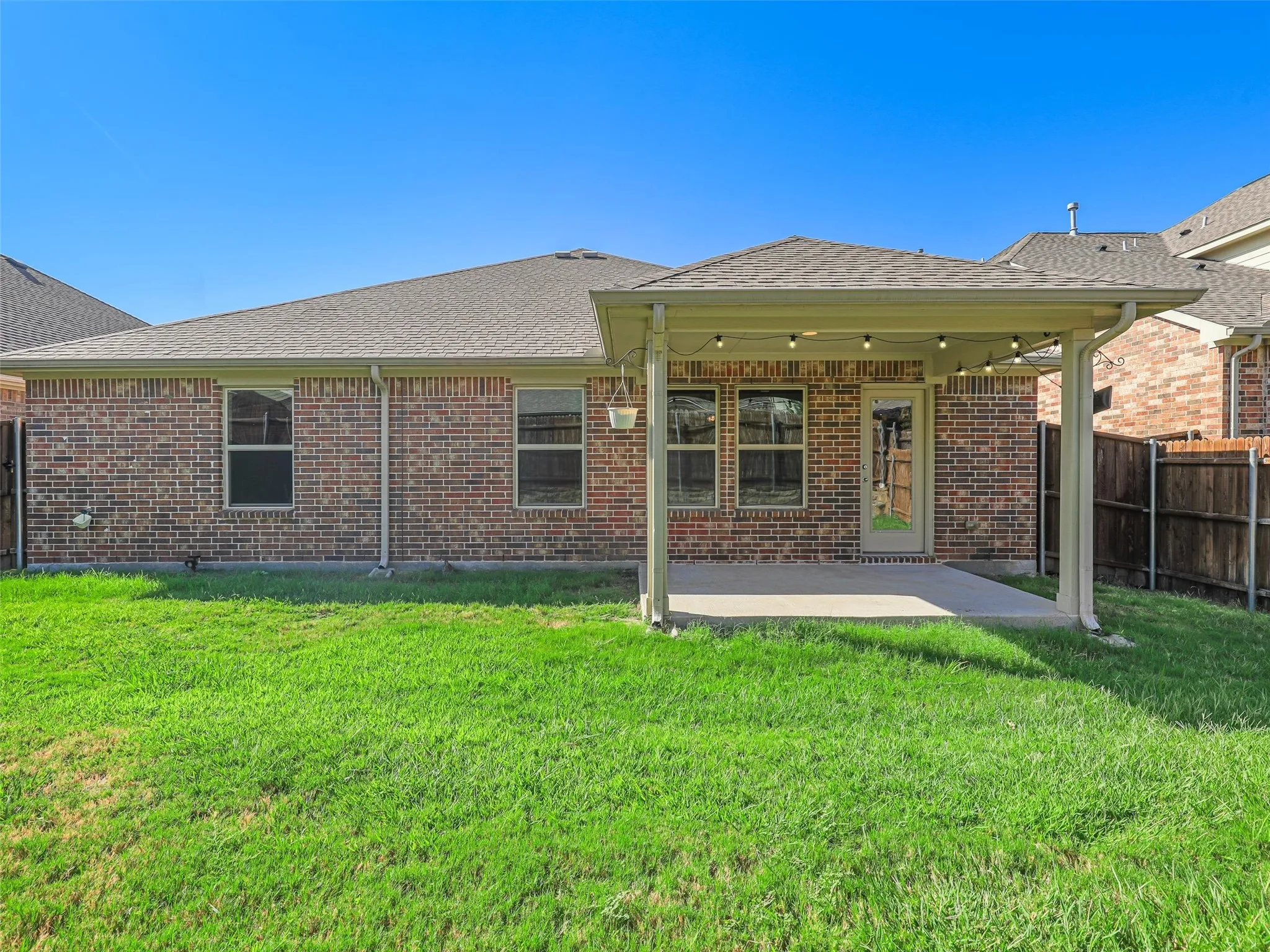 Expansive green lawn with a covered patio, brick exterior, and privacy fencing