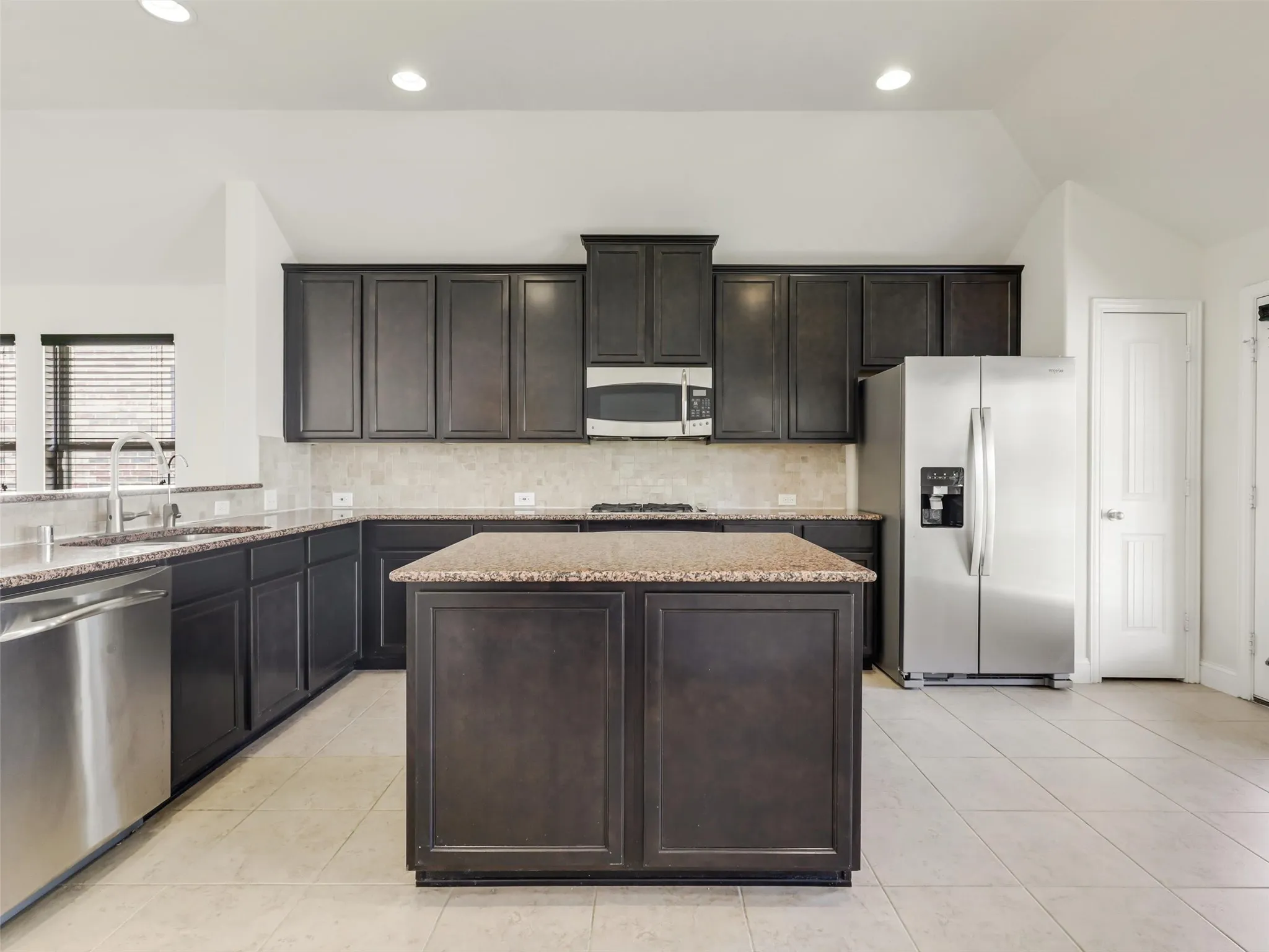 Kitchen featuring a central island, dark wood cabinetry, granite countertops, tile backsplash, and stainless steel appliances