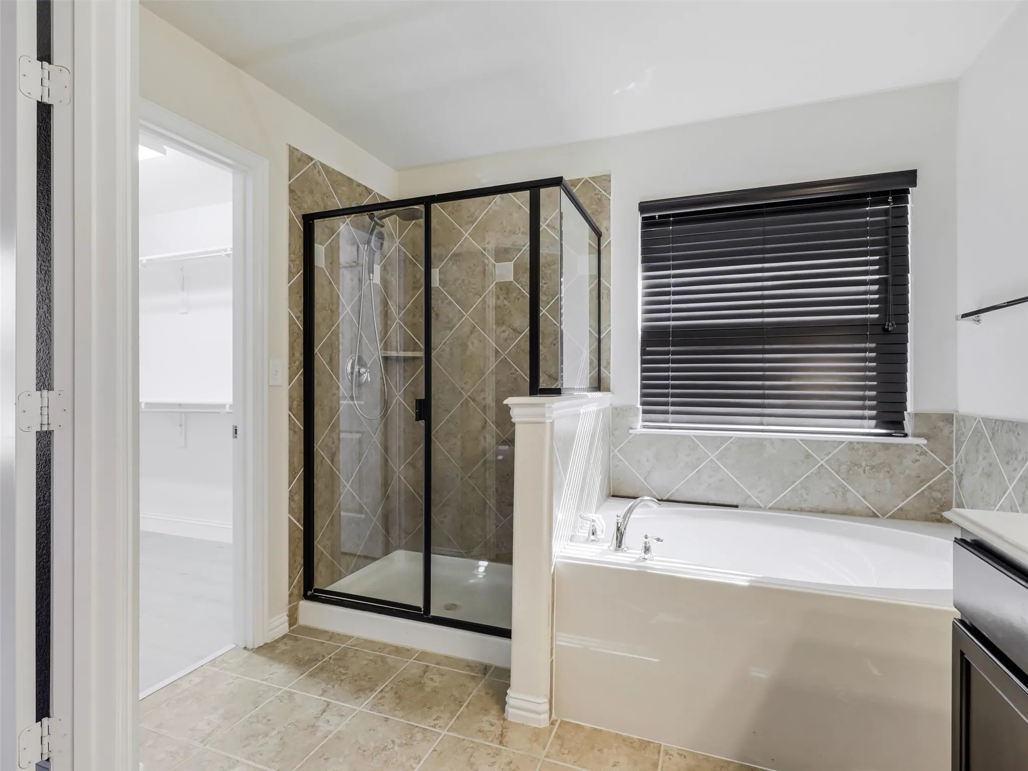 Soaking tub, walk-in shower with glass enclosure, tiled shower surround, tiled flooring, and window with blinds