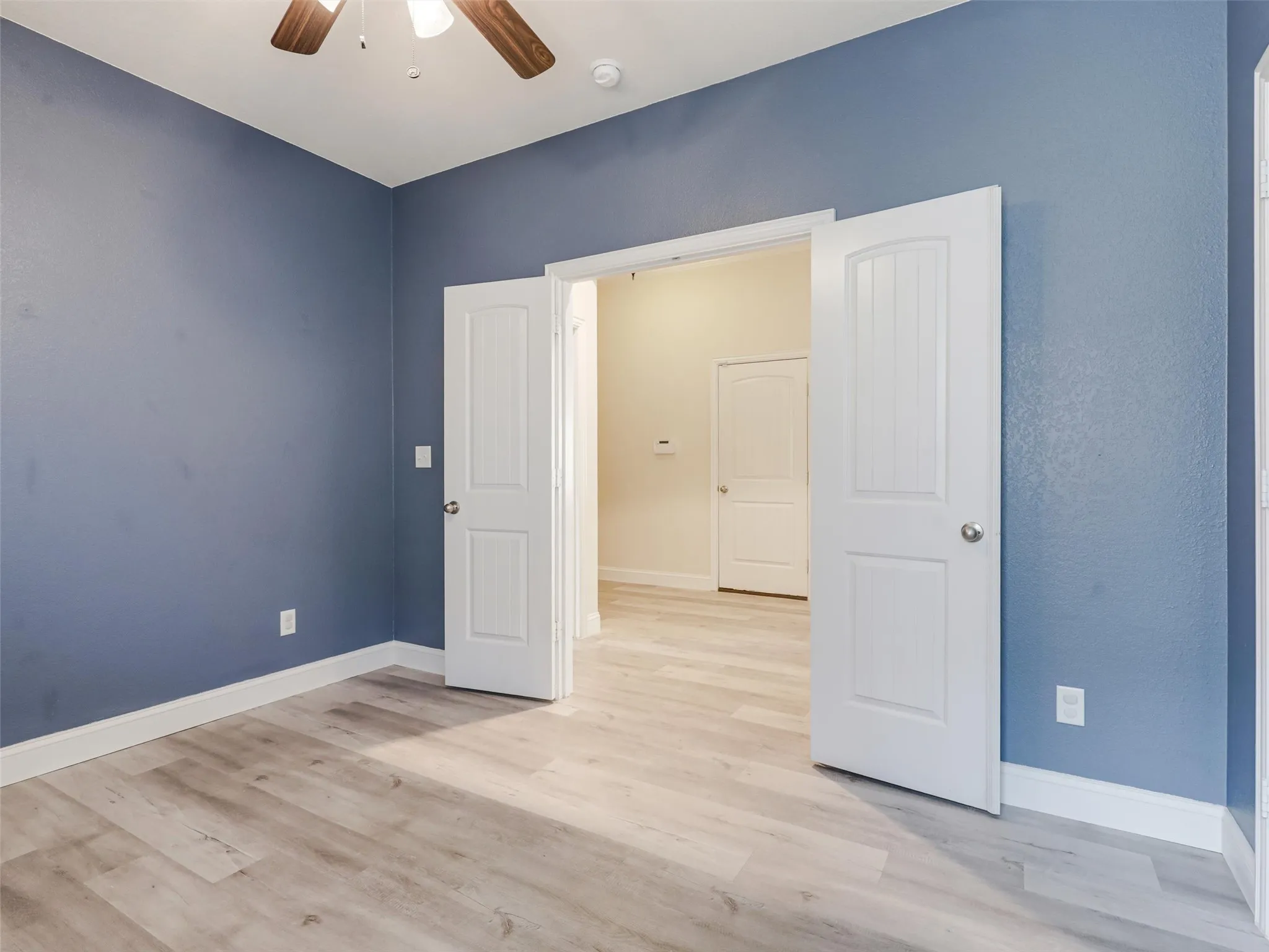Wood-finish flooring, blue painted walls, white trim, and a ceiling fan with wood-finish blades