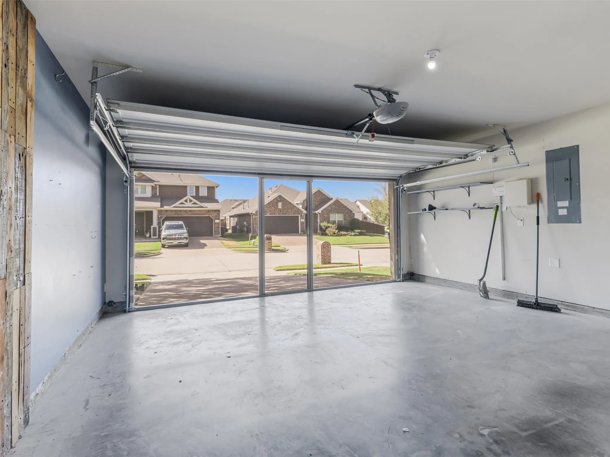 Spacious garage with an automatic roll-up door, exposed concrete flooring, and built-in wall shelving