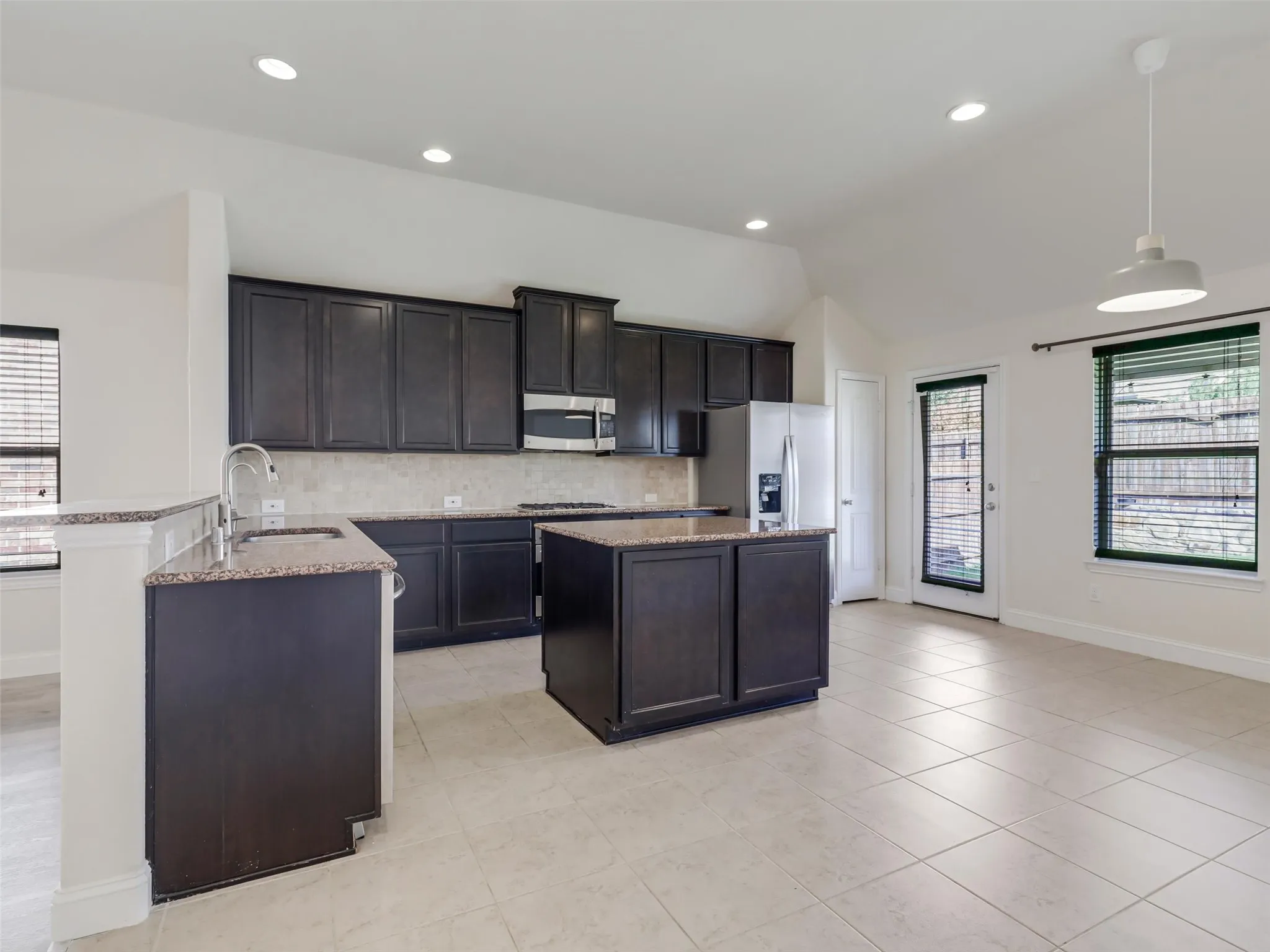 Spacious kitchen featuring dark wood cabinetry, granite countertops, stainless steel appliances, a center island, and tile flooring