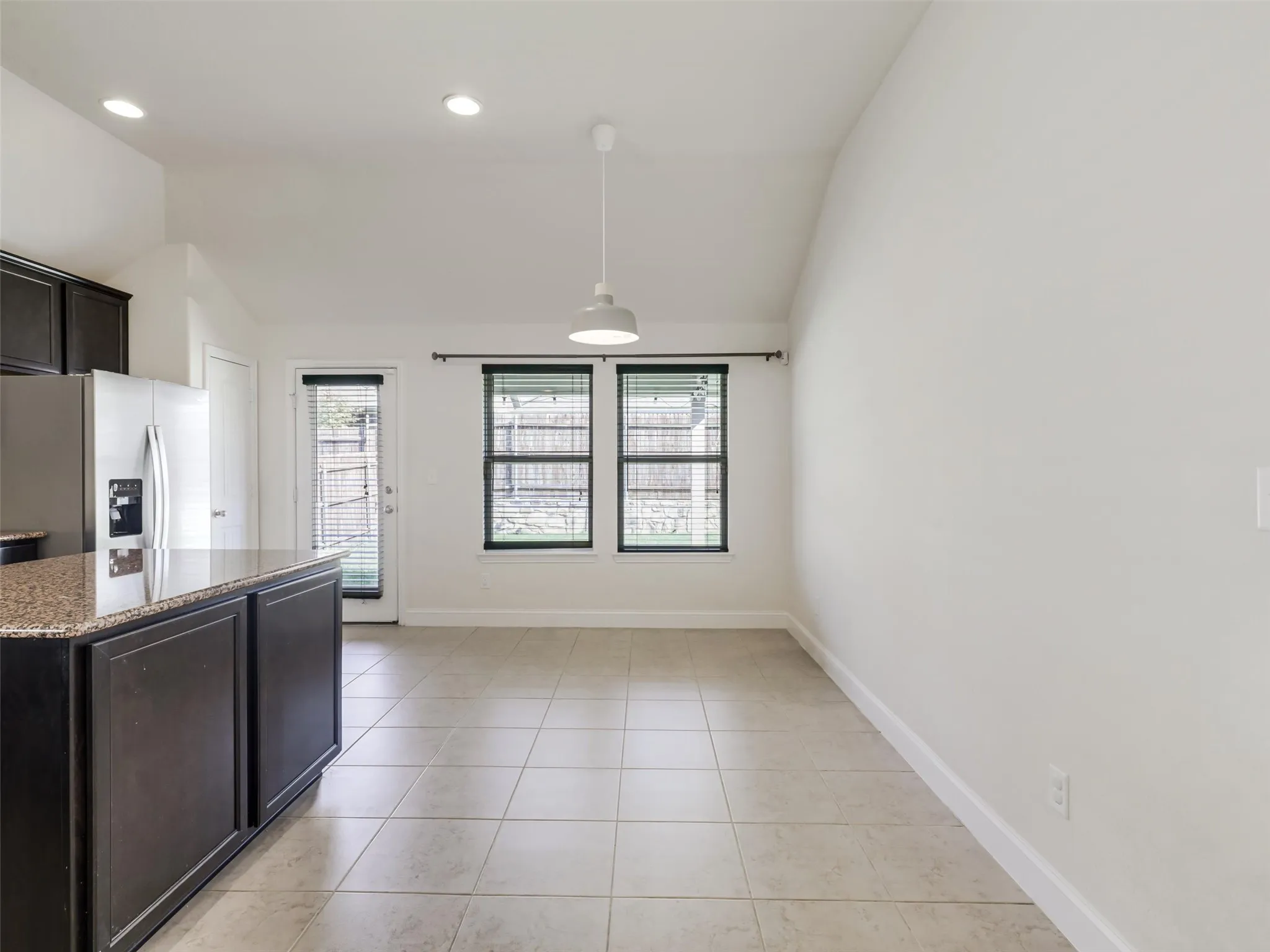 Kitchen and dining area featuring a vaulted ceiling, recessed lighting, tile flooring, and a kitchen island with a stone countertop