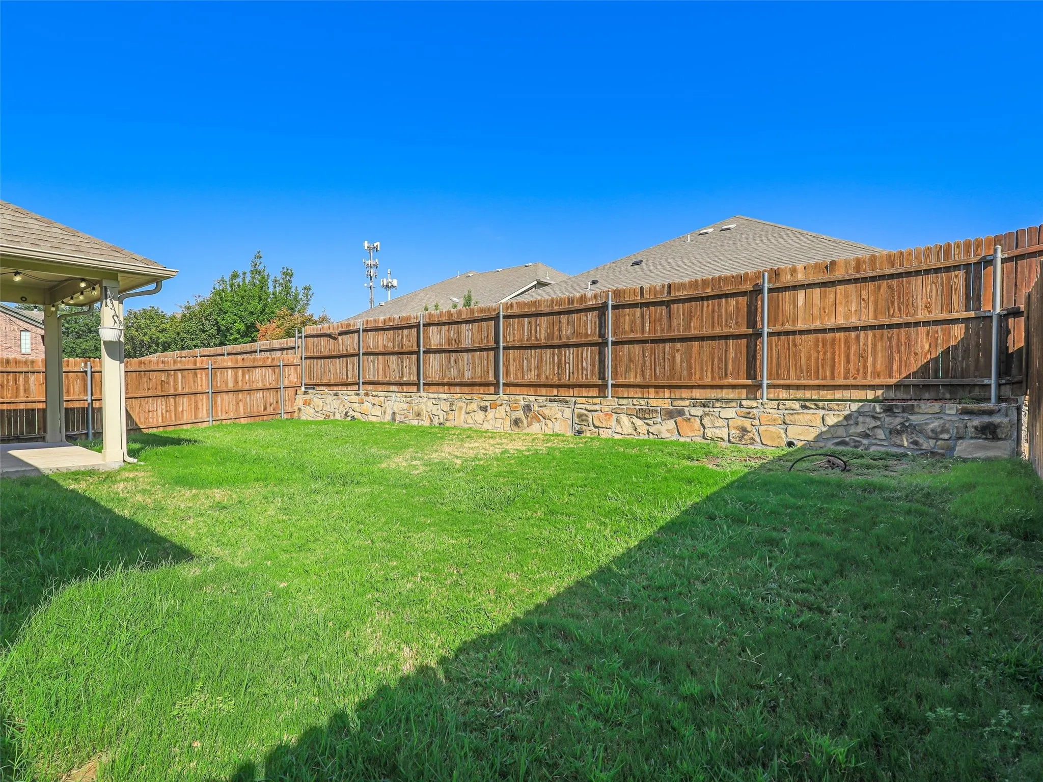 Expansive backyard featuring a manicured lawn, wood privacy fencing, and a stone retaining wall