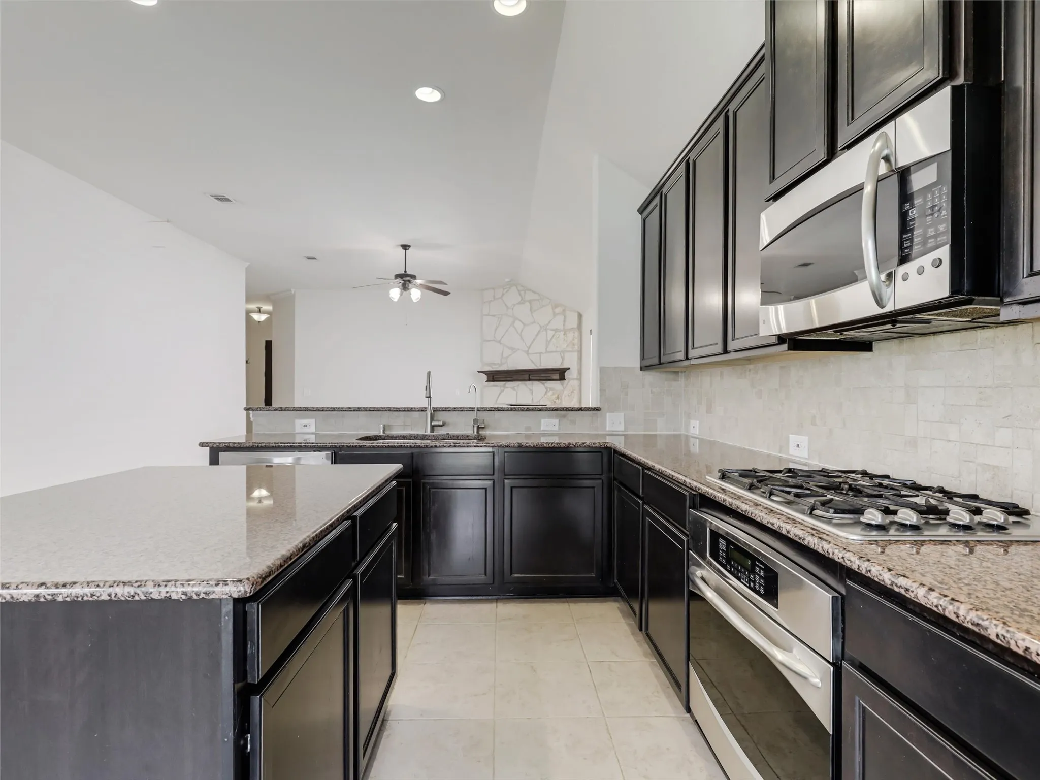 Kitchen featuring dark wood-finish cabinetry, light speckled countertops, a tile backsplash, stainless steel appliances, and tile flooring
