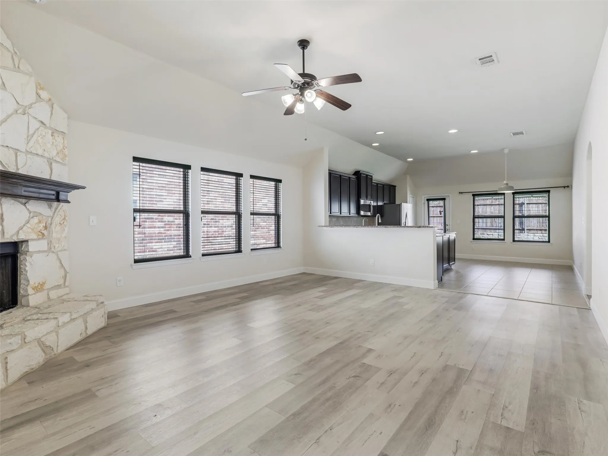 Open-concept living space featuring wood-finish flooring, a stone fireplace, vaulted ceilings, a ceiling fan, and recessed lighting