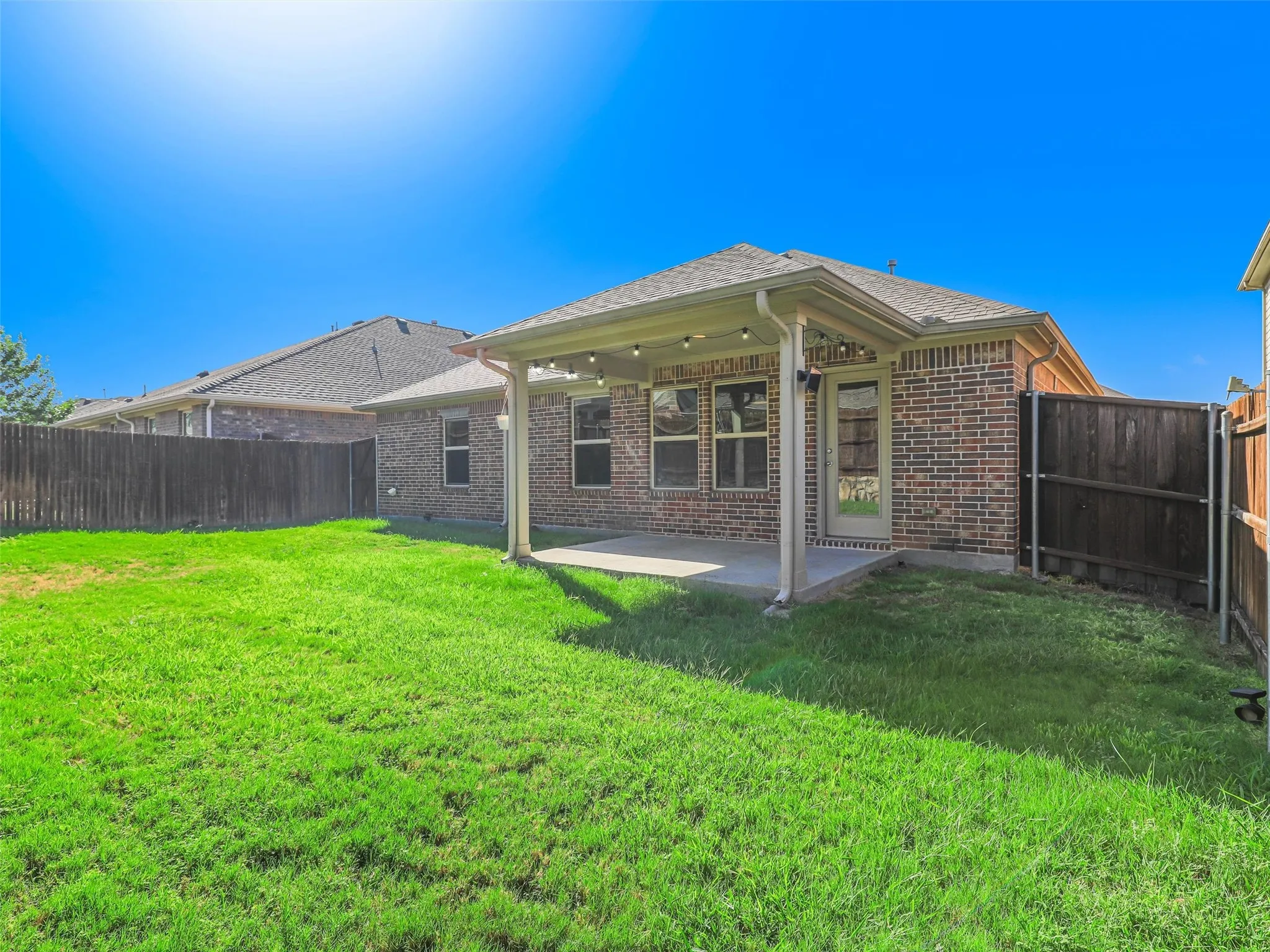 Expansive green lawn with a covered patio, brick exterior, and full wood fencing