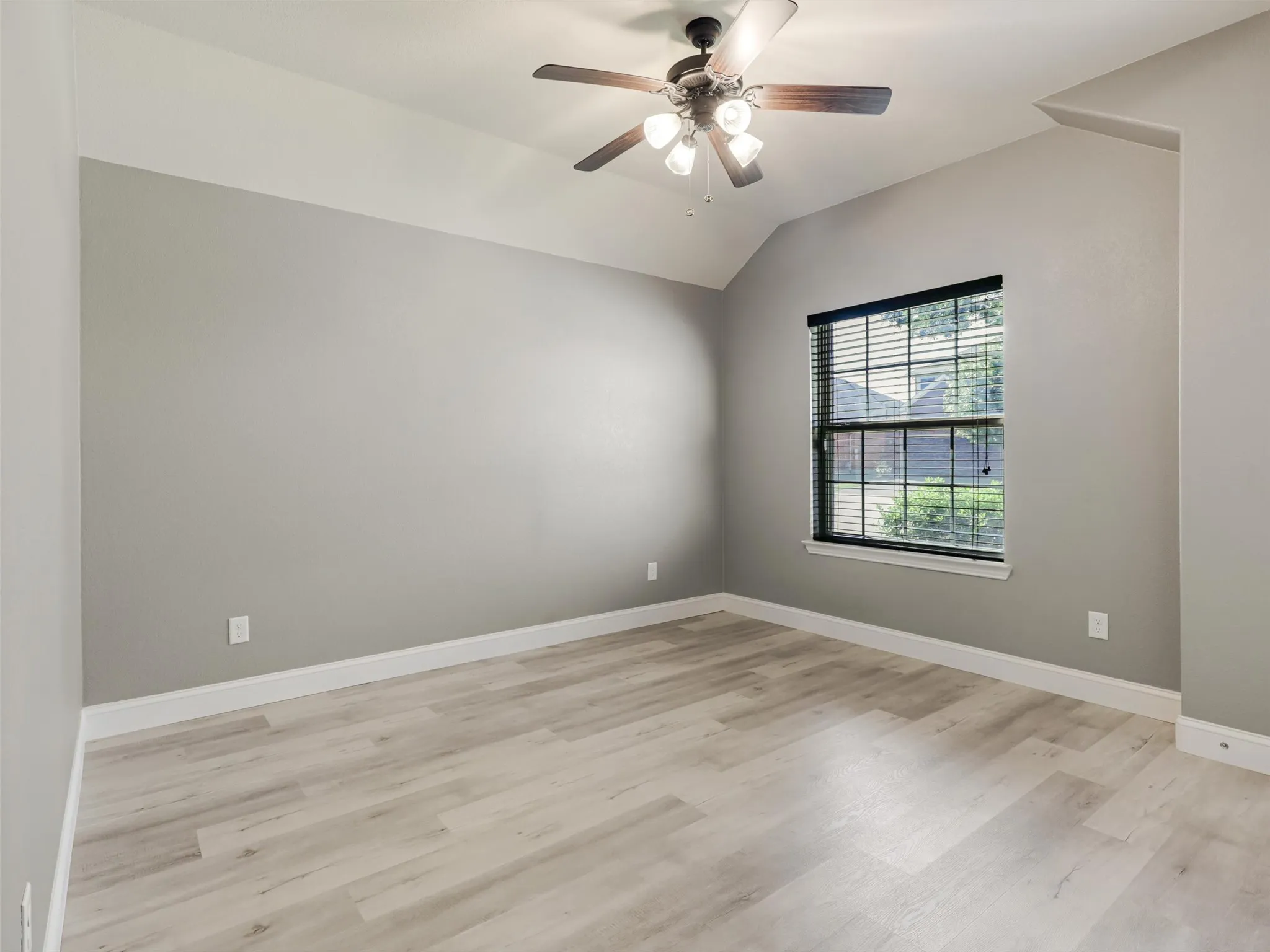 Vaulted ceiling, wood-finish flooring, ceiling fan with integrated lighting, window with blinds, neutral wall tones