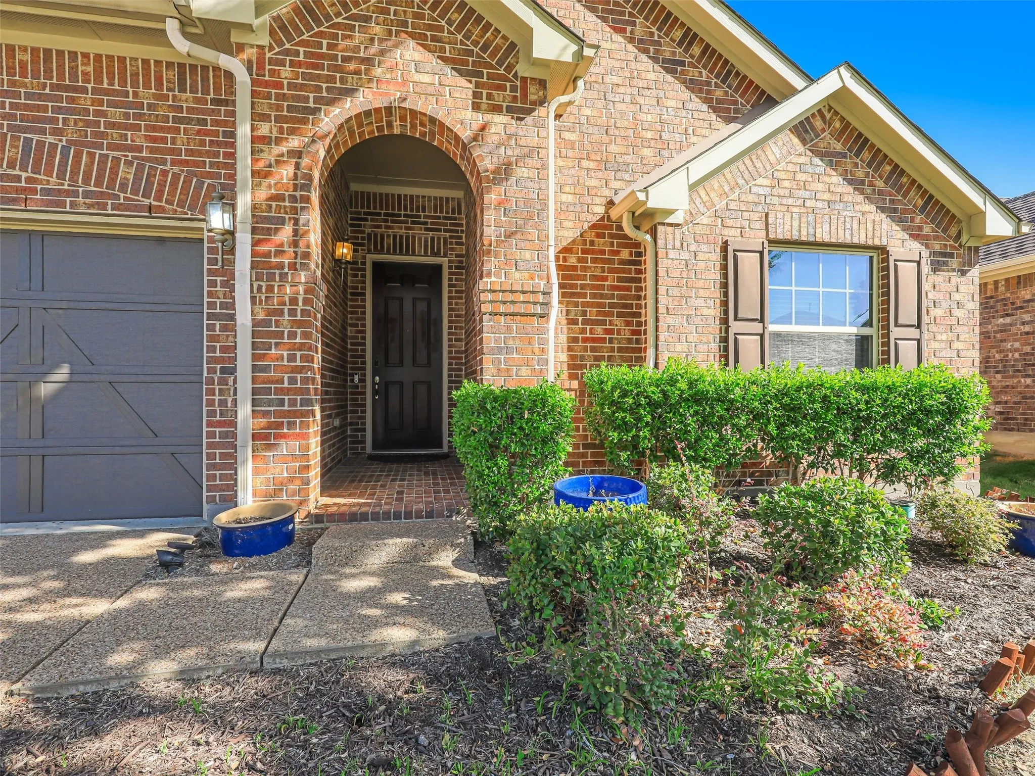 Brick exterior with an arched entry, dark panel front door, and a single window with louvered shutters