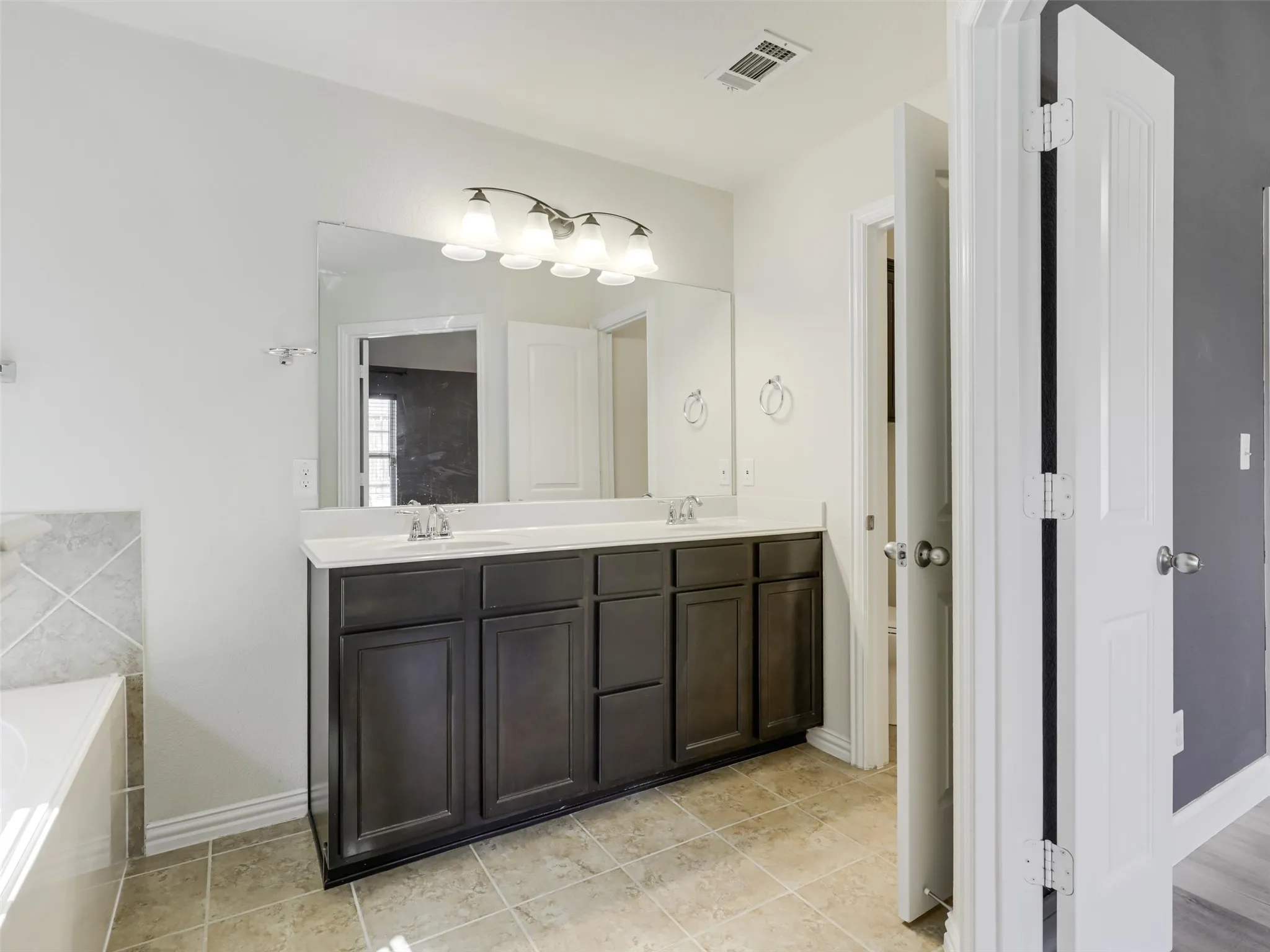 Double vanity with dark wood-finish cabinetry, integrated sinks, and a large wall-mounted mirror