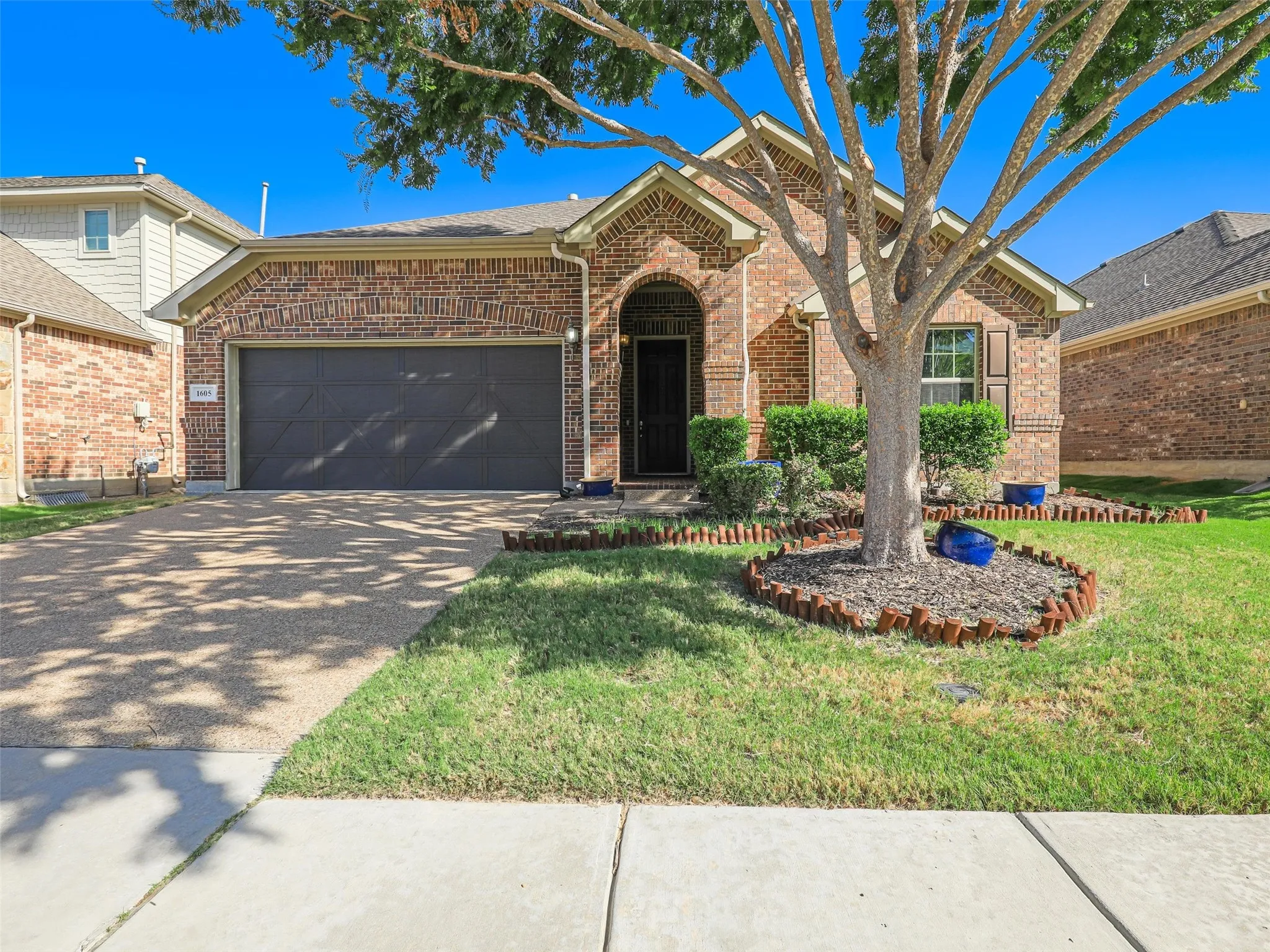 Brick exterior with an arched entry, dark garage door, and a concrete driveway