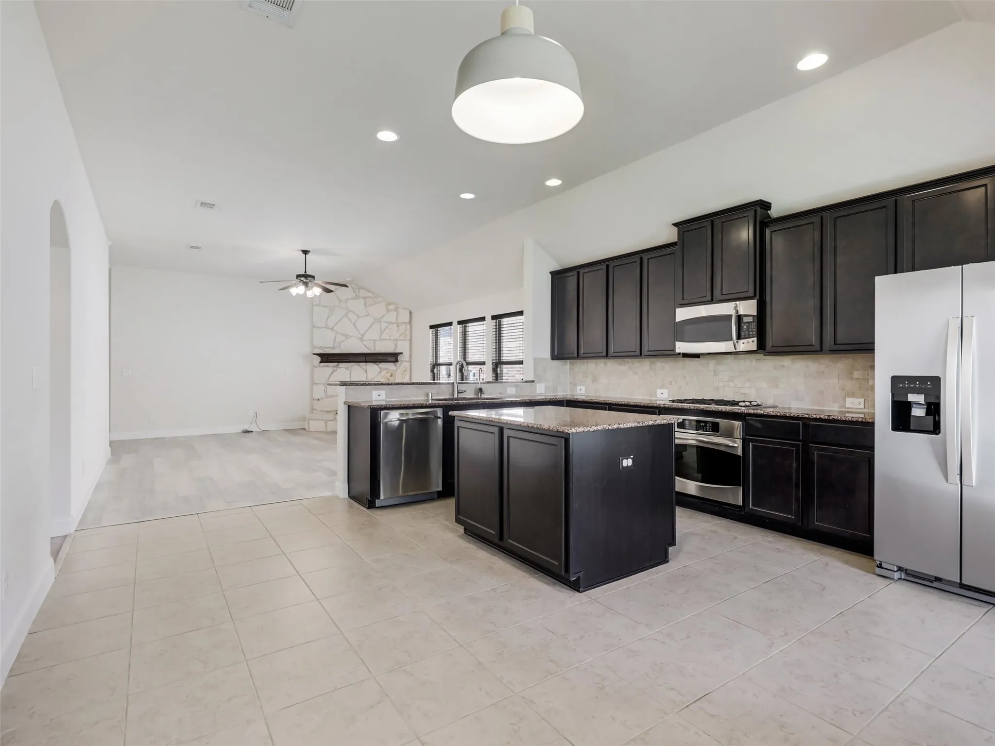 Kitchen featuring dark wood cabinetry, stainless steel appliances, a center island with a stone countertop, and tile flooring