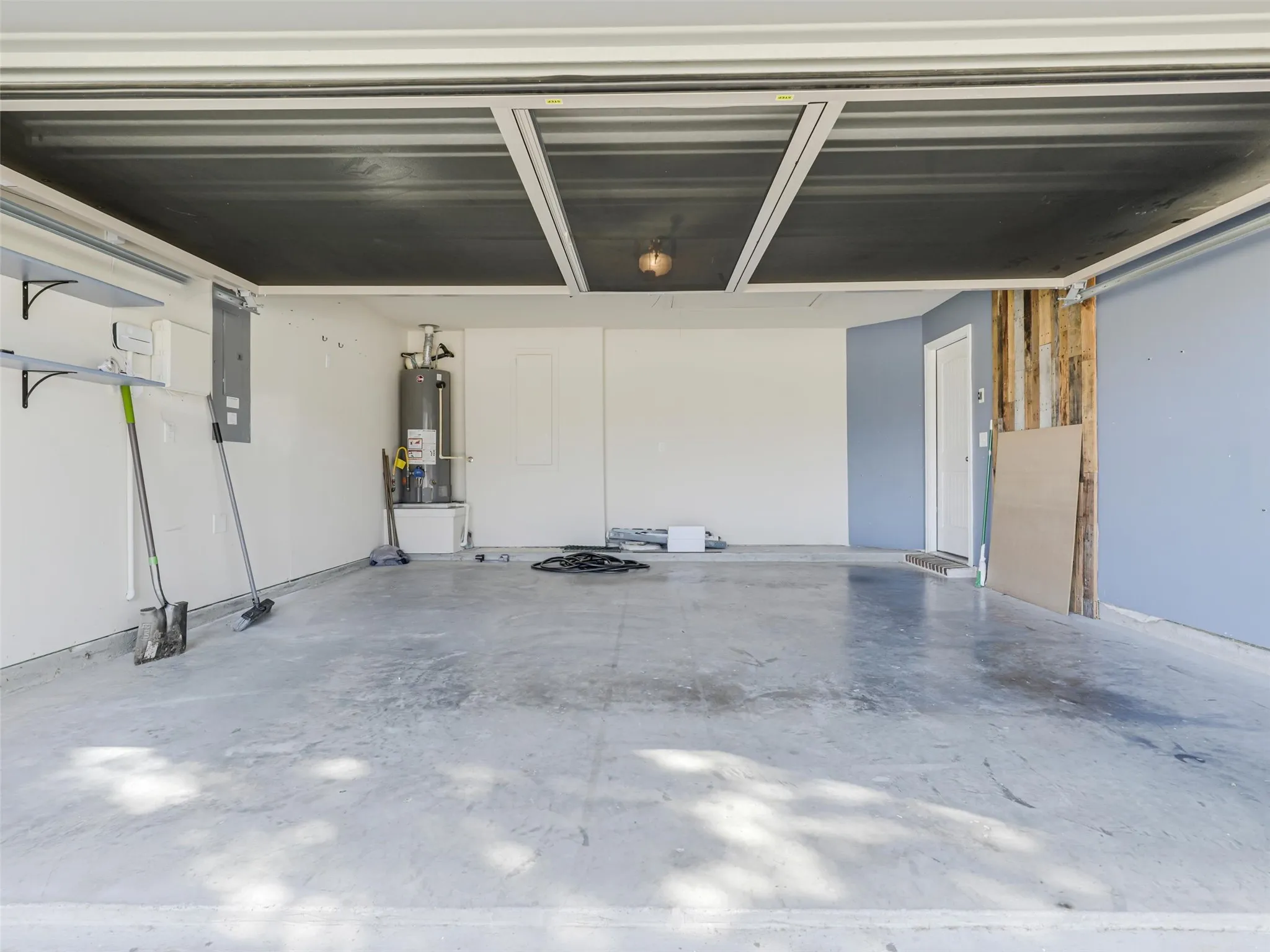 Spacious garage with concrete flooring, overhead light fixture, exposed wood wall elements, and built-in shelving