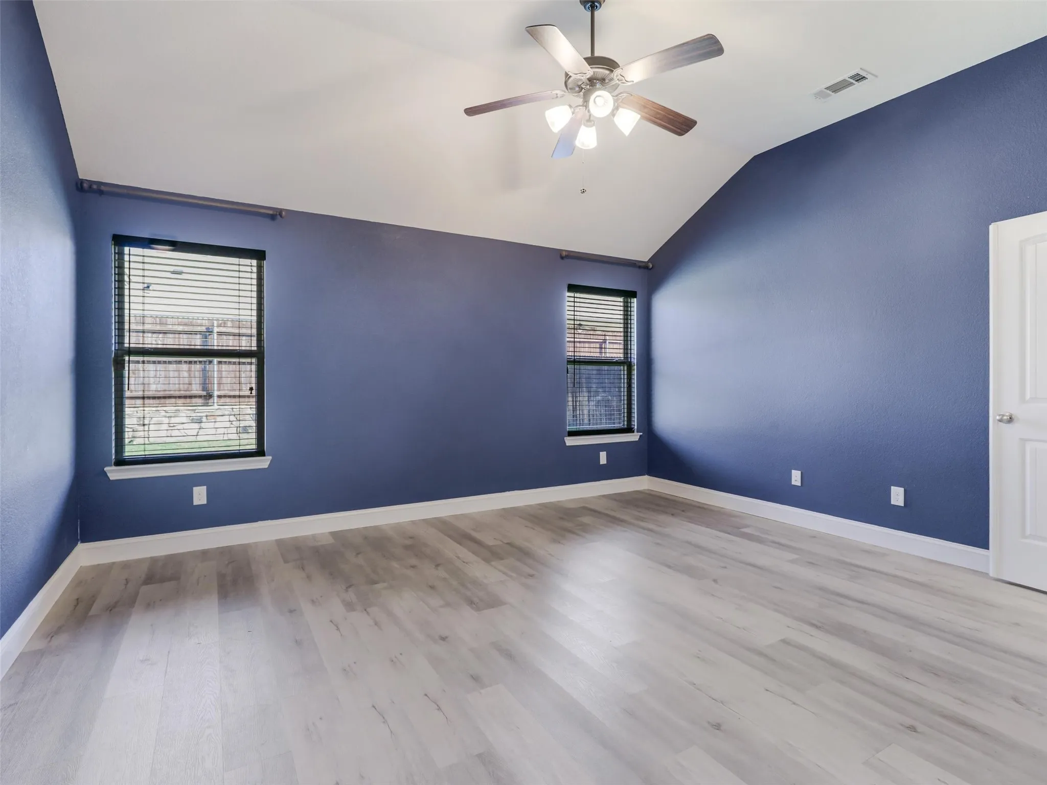 Vaulted ceiling with a ceiling fan, two windows, and light wood-finish flooring