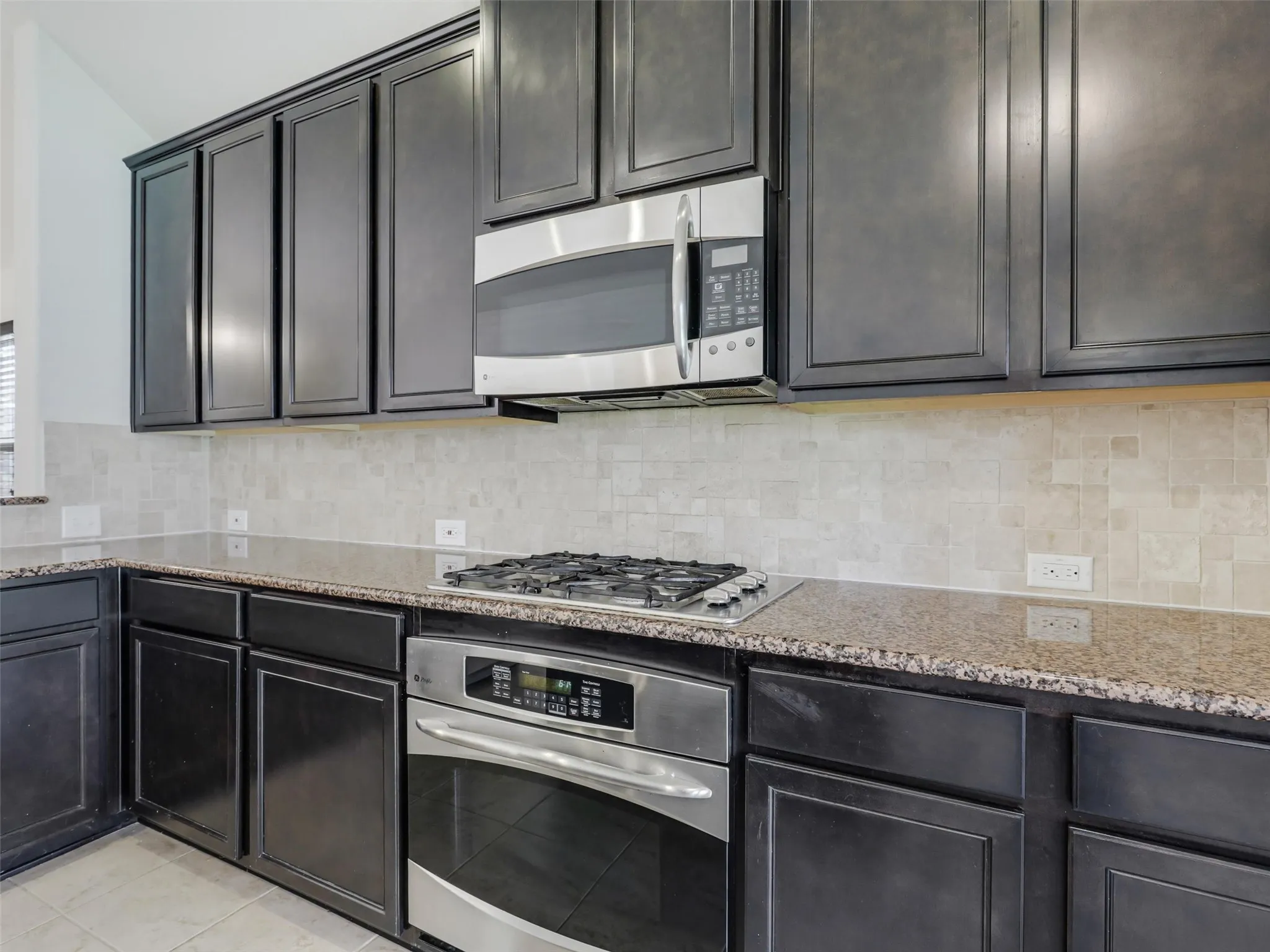 Stainless steel microwave, gas cooktop, built-in oven, dark wood-finish cabinetry, and stone countertops