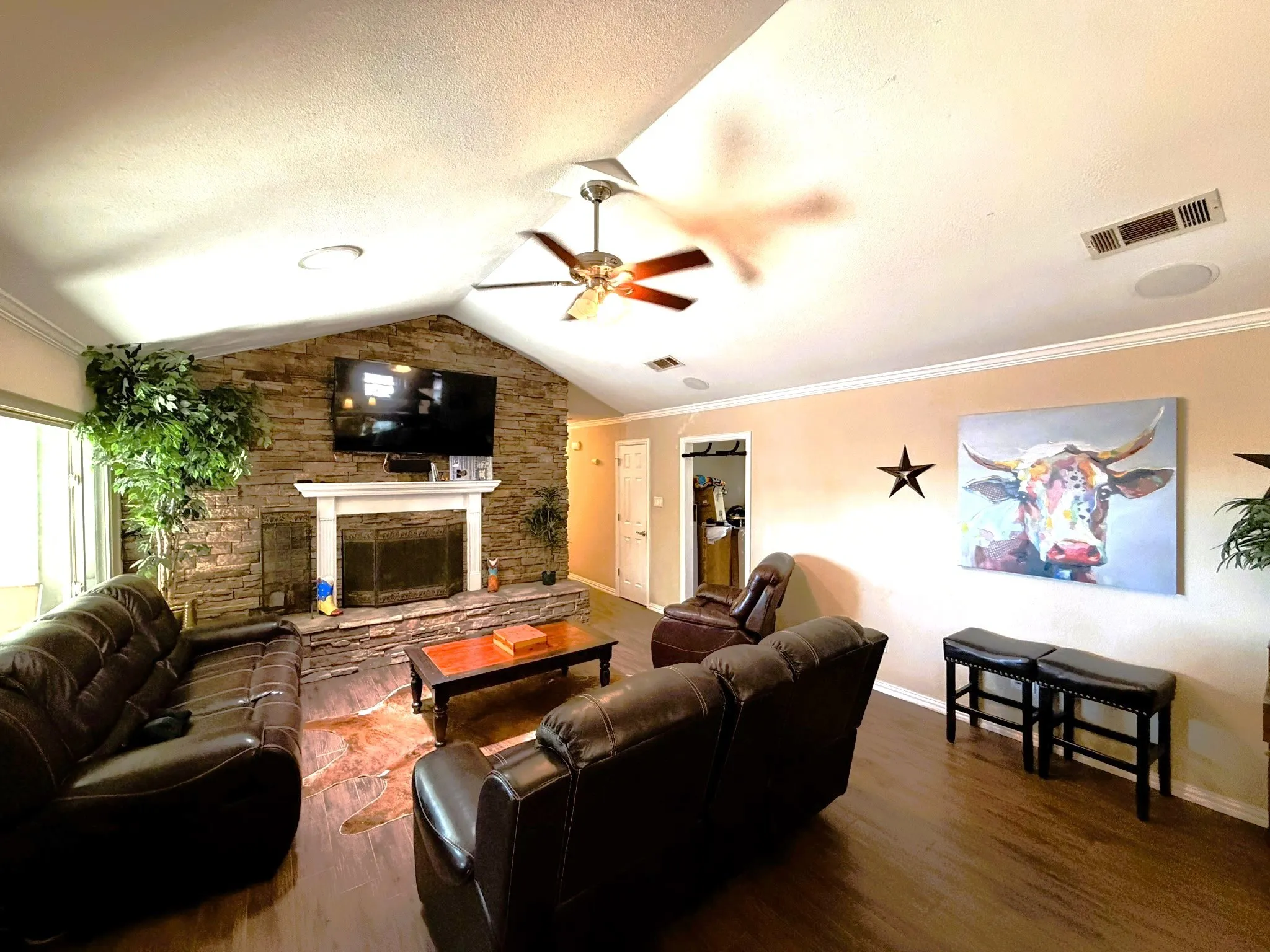 Vaulted ceiling, stone-clad fireplace with mantel, wood-finish flooring, ceiling fan, and crown molding